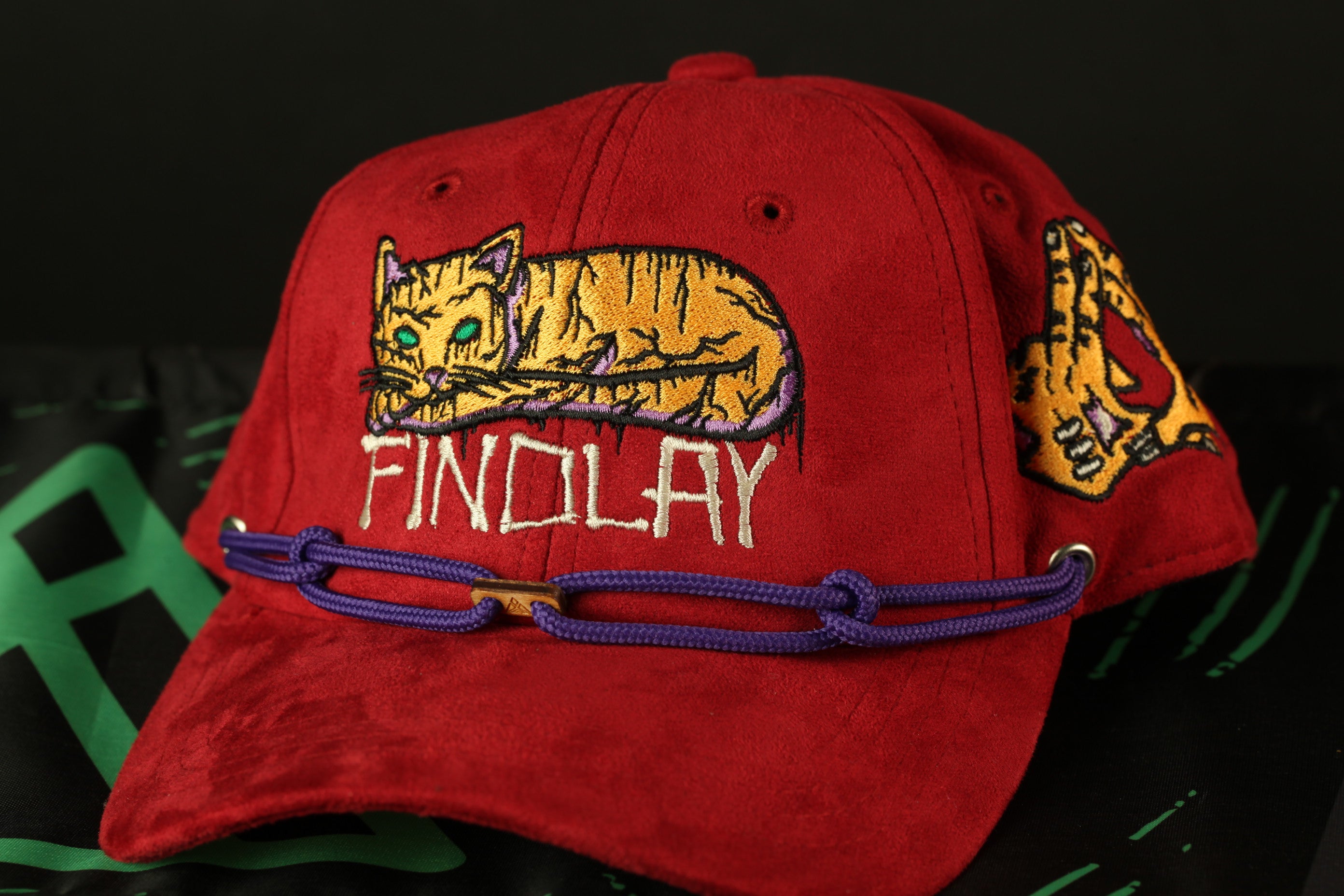 A red baseball cap with a cat embroidered on it, and the word "FINDOLAY" written on it.