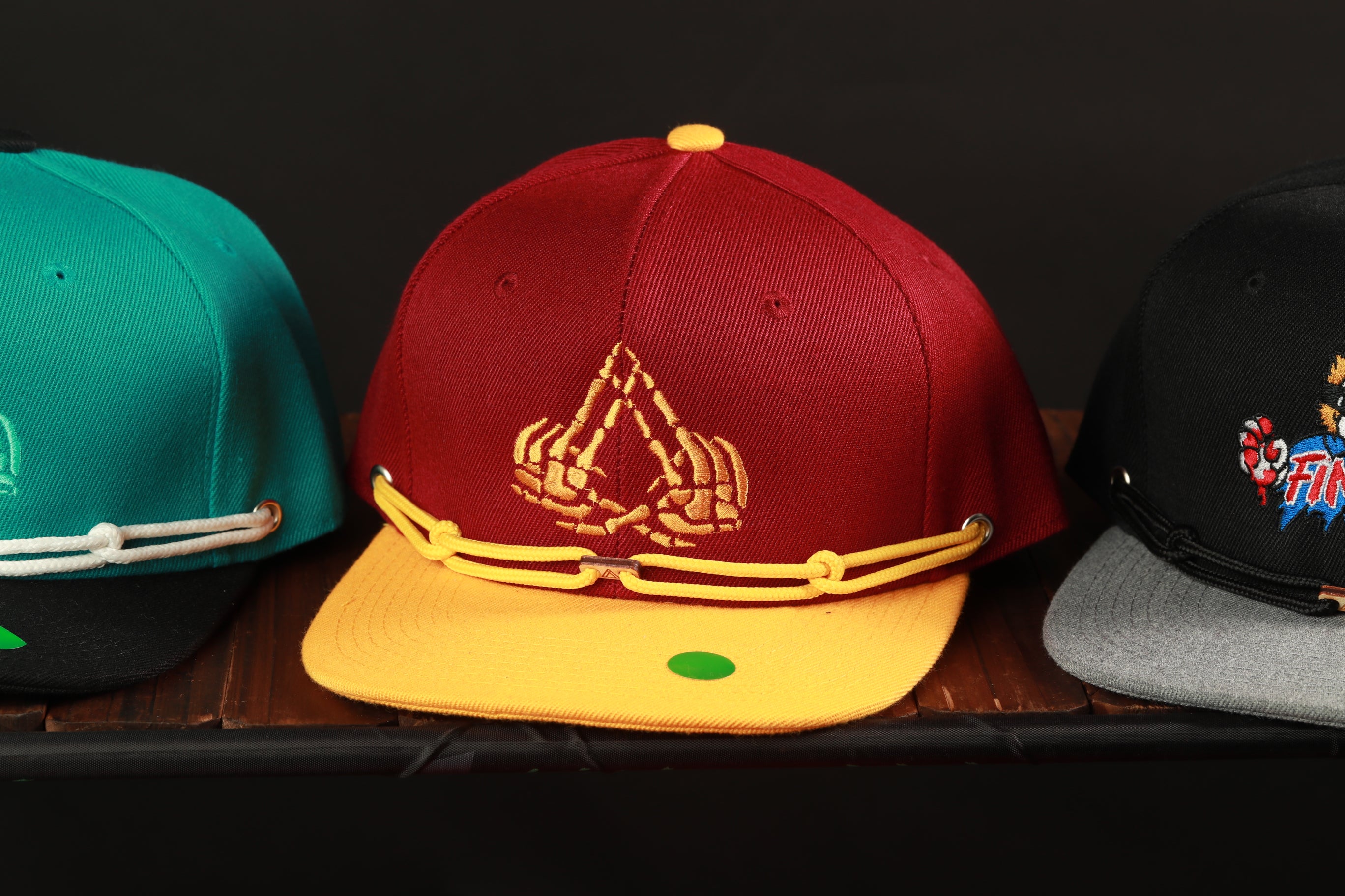 Three baseball caps are displayed on a wooden surface, each with a unique design and color.