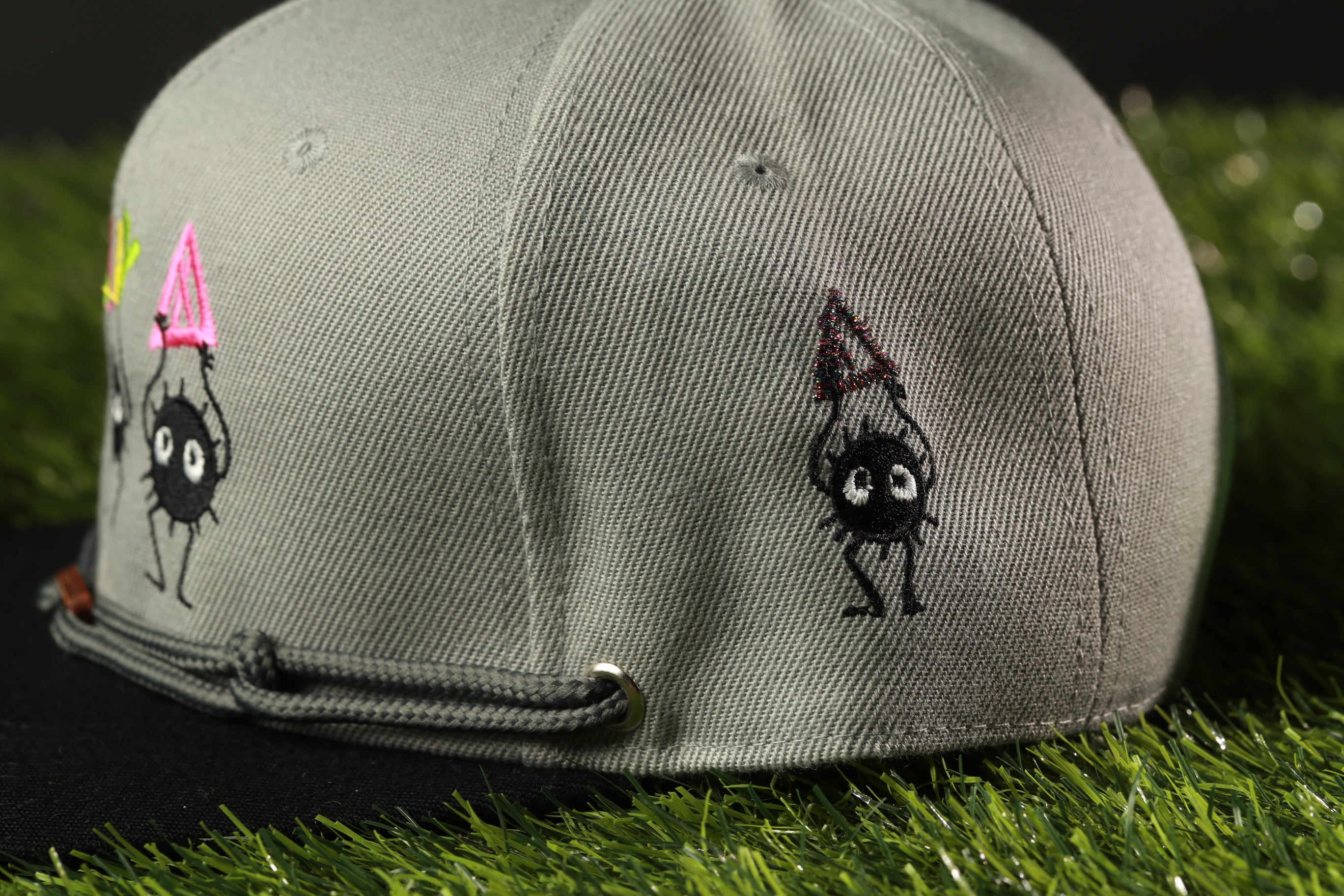 A gray baseball cap with a cartoon character design on it, sitting on a grassy surface.