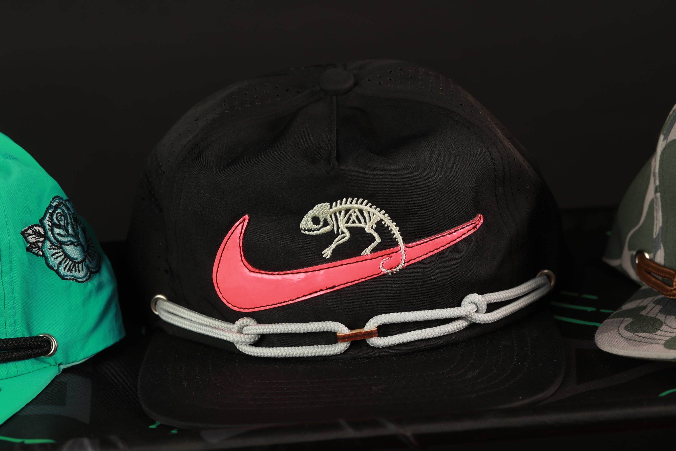 A black baseball cap with a pink Nike swoosh and a skeleton design on the front.