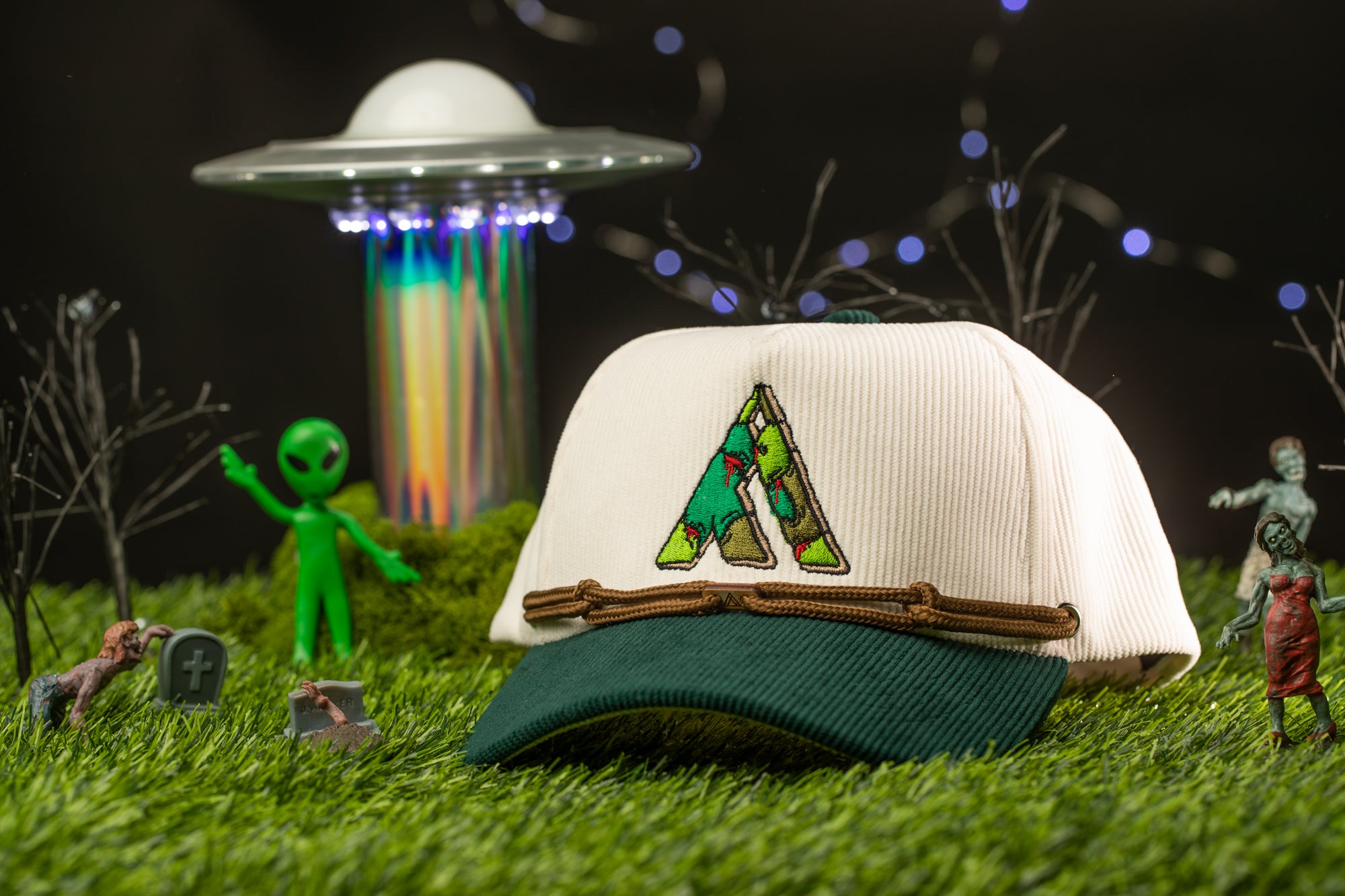 a green alien figurine, a white baseball cap with a green and brown design, and various small toy figures and objects arranged on a grassy surface.