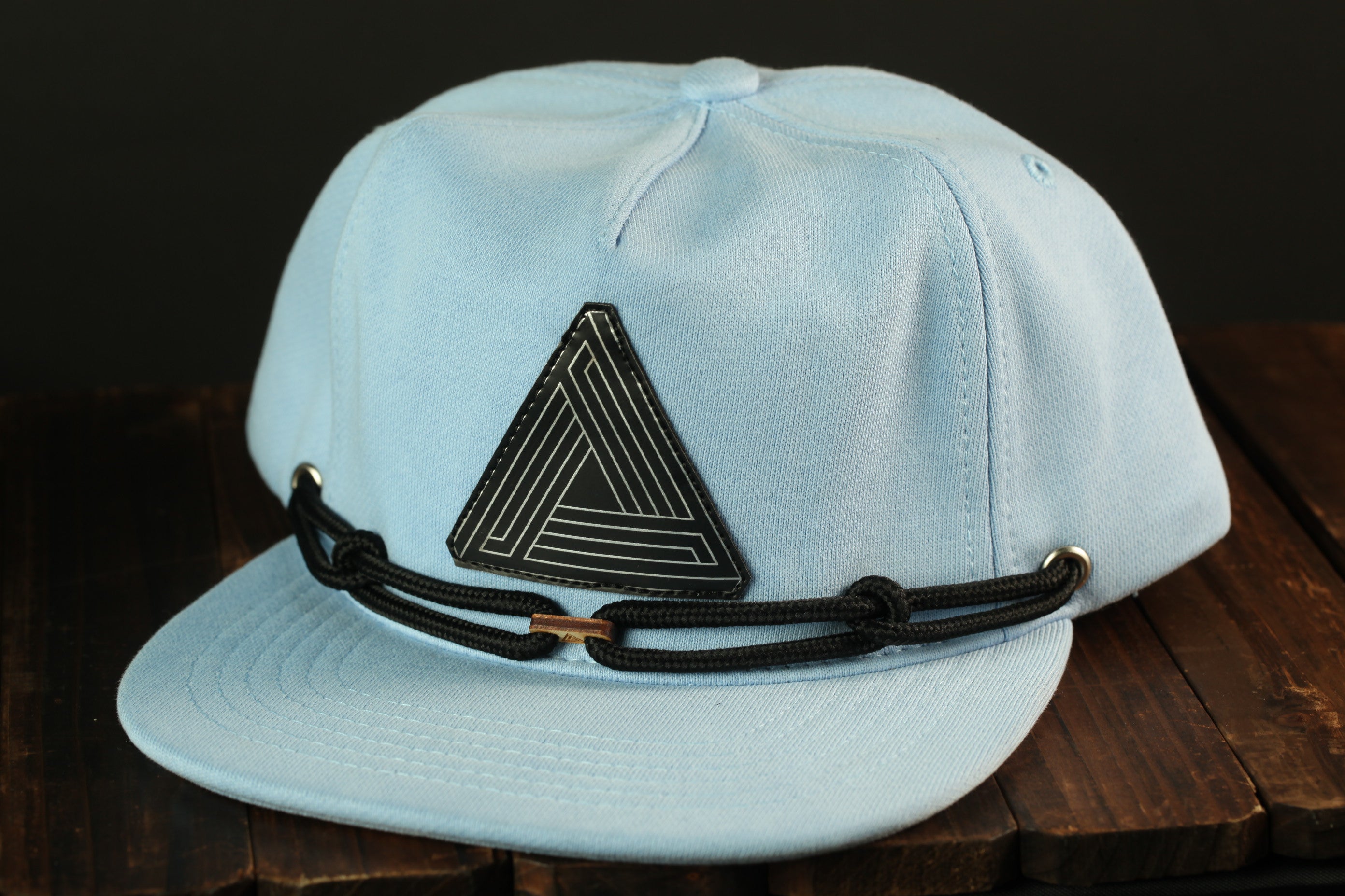 A light blue baseball cap with a black geometric pattern on the front, sitting on a wooden surface.