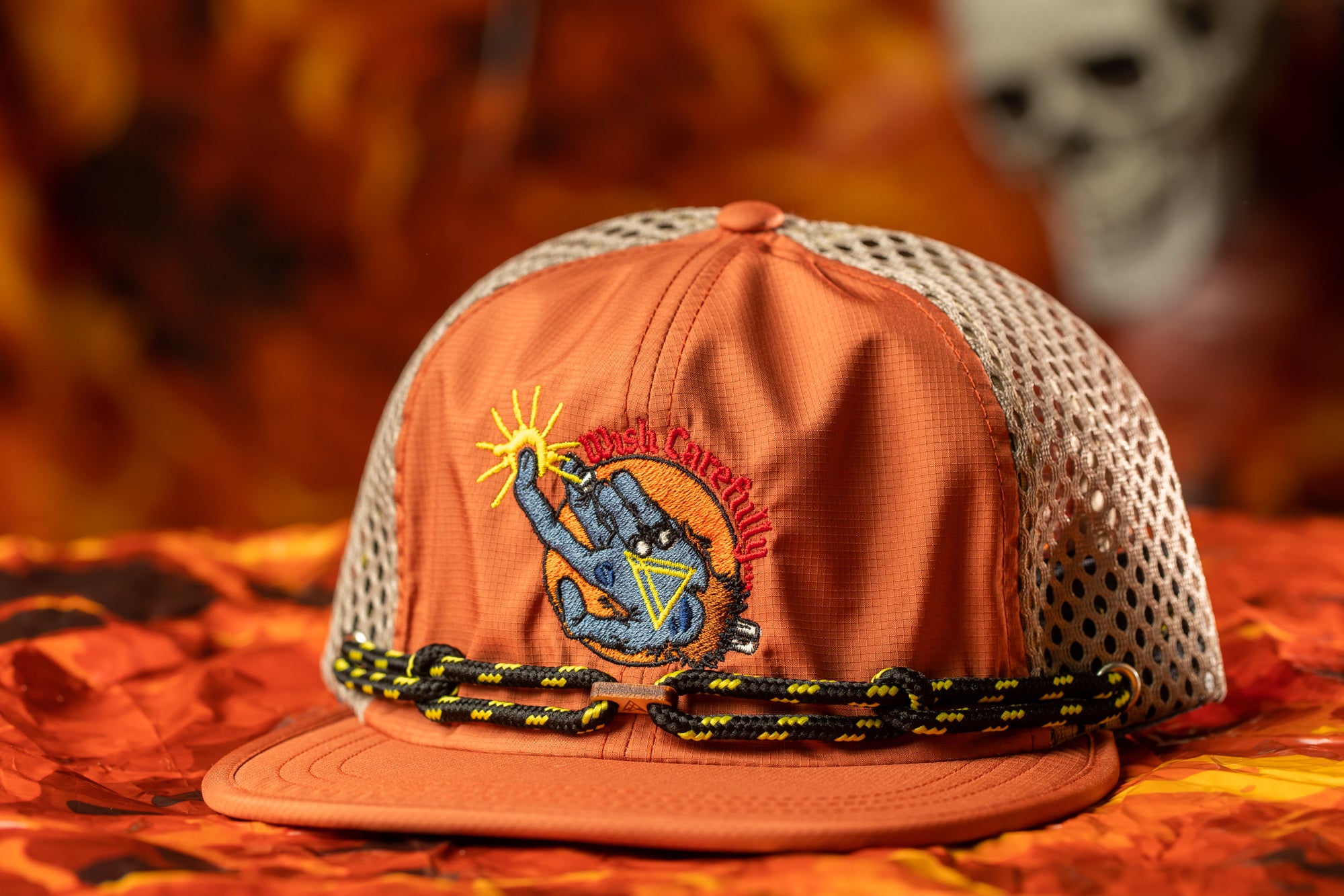 An orange baseball cap with a mesh back and a graphic design on the front, placed on a surface with a blurred background.