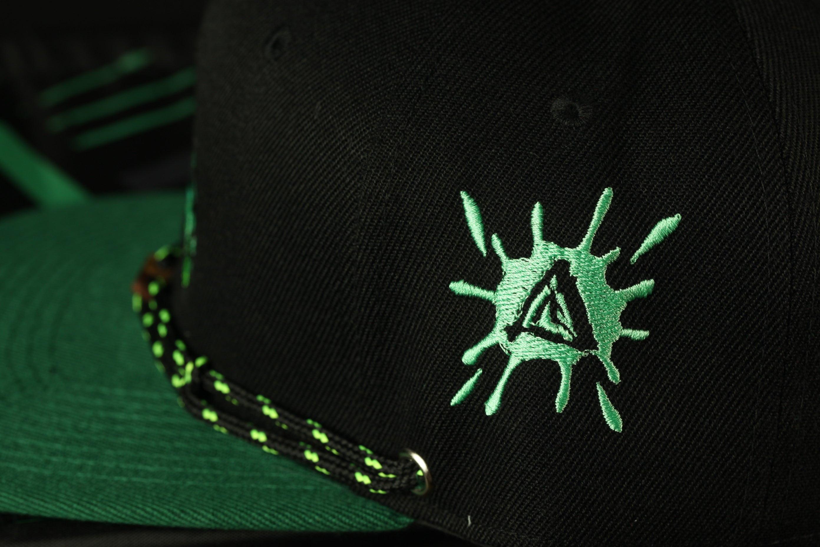 A close-up view of a black baseball cap with a green and black embroidered logo on the front.