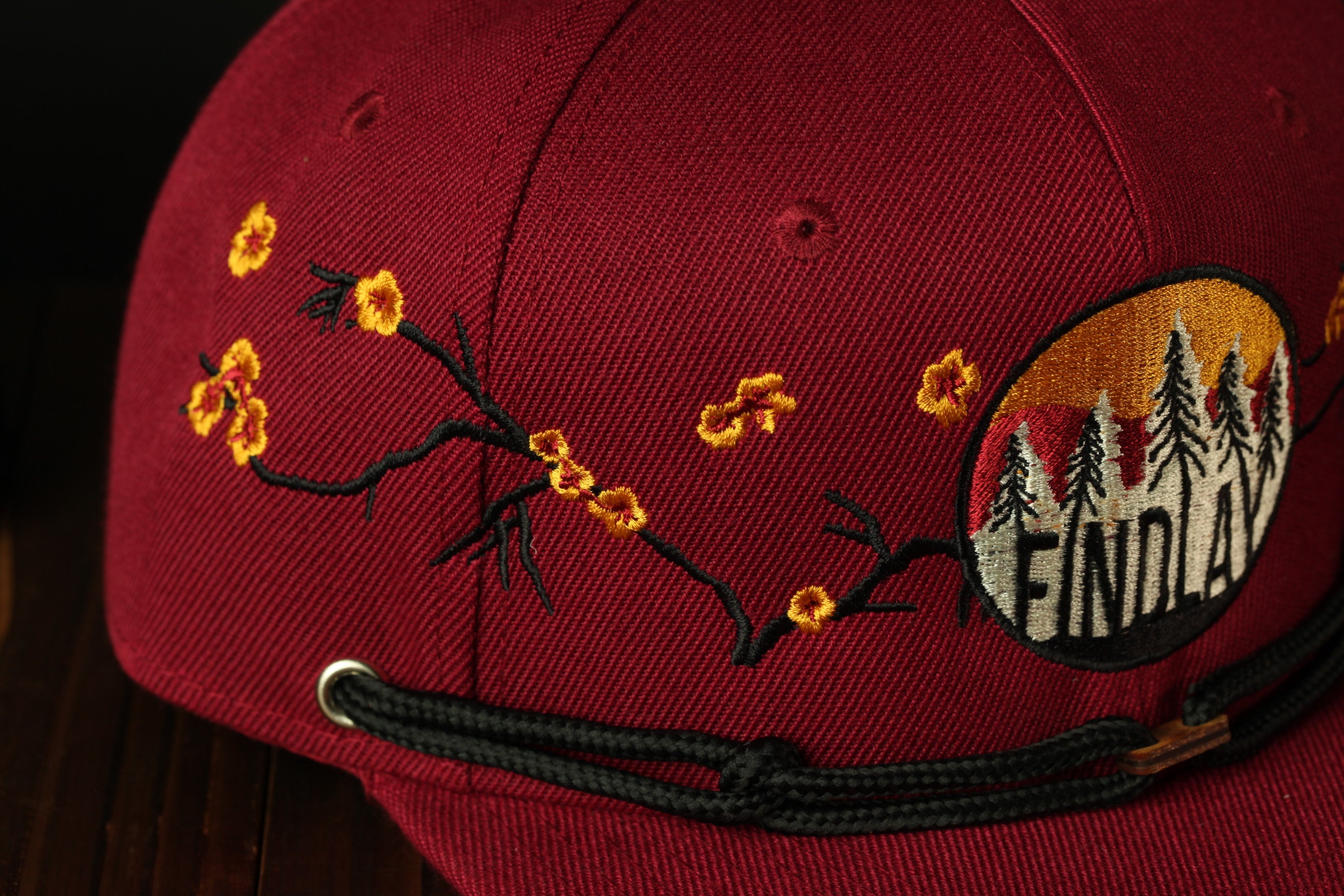 A close-up view of a maroon baseball cap with a floral embroidered design and the word "ENDLAY" on it.