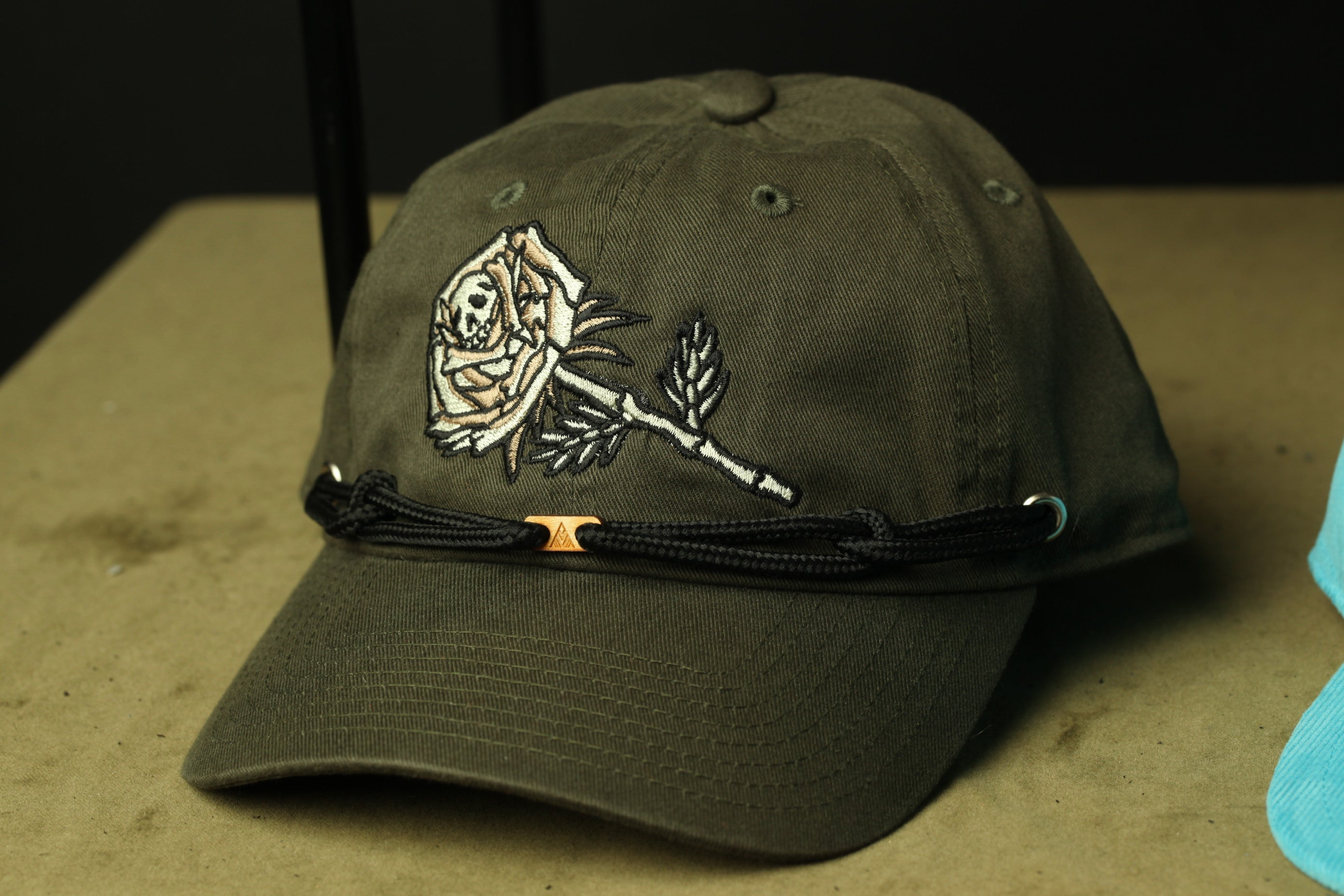 A dark green baseball cap with a rose embroidered on the front, resting on a surface.