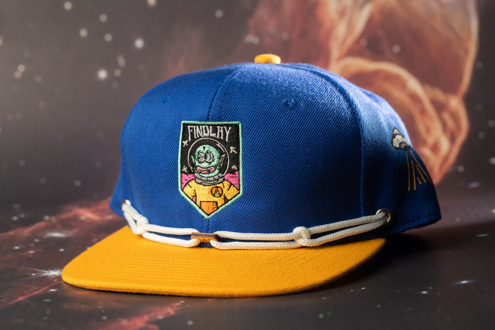 A blue baseball cap with a yellow brim, featuring a colorful patch with a cartoon character and the text "Findlay" on the front.