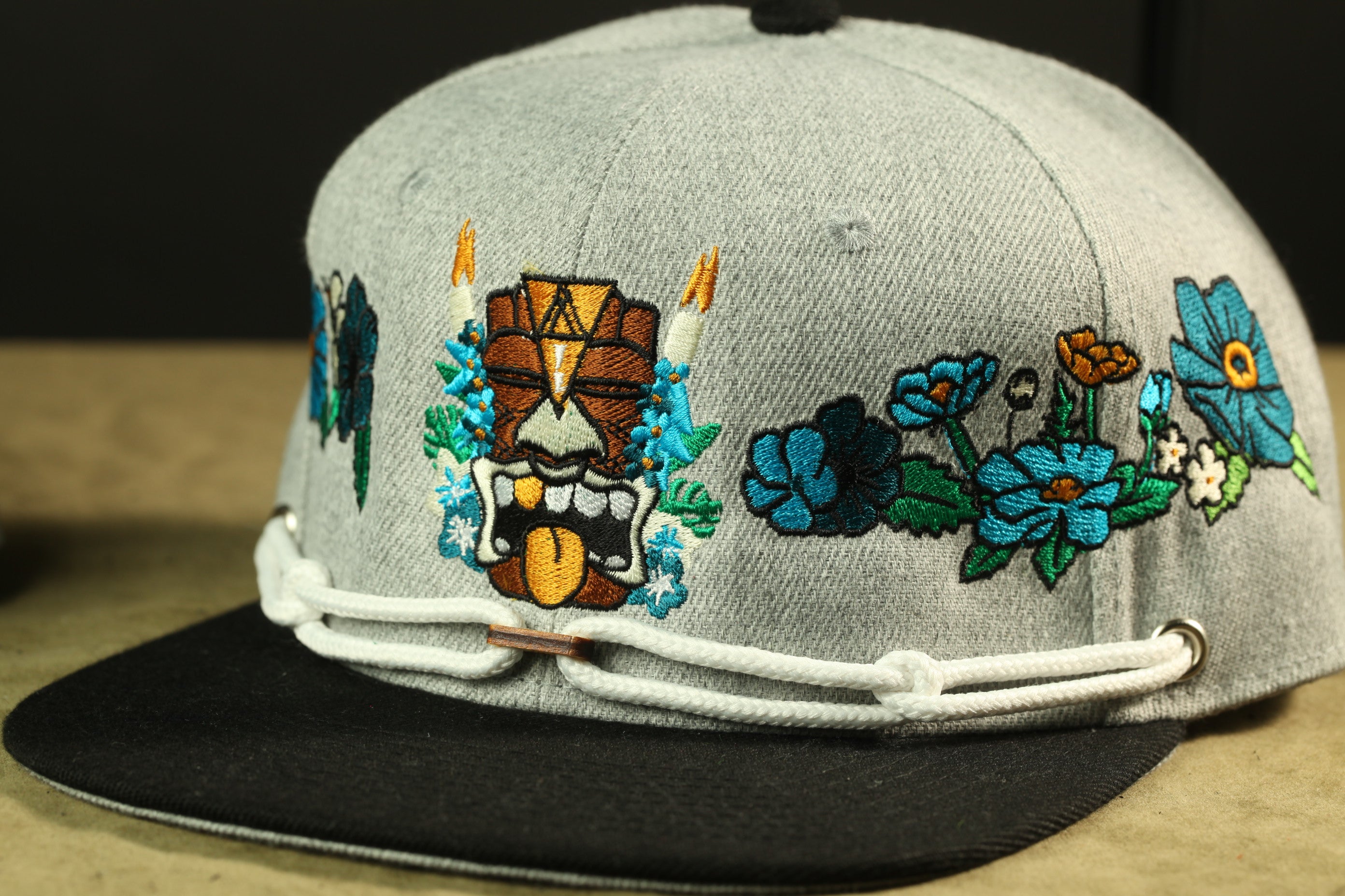 A gray baseball cap with colorful floral embroidery and a tiki mask design.