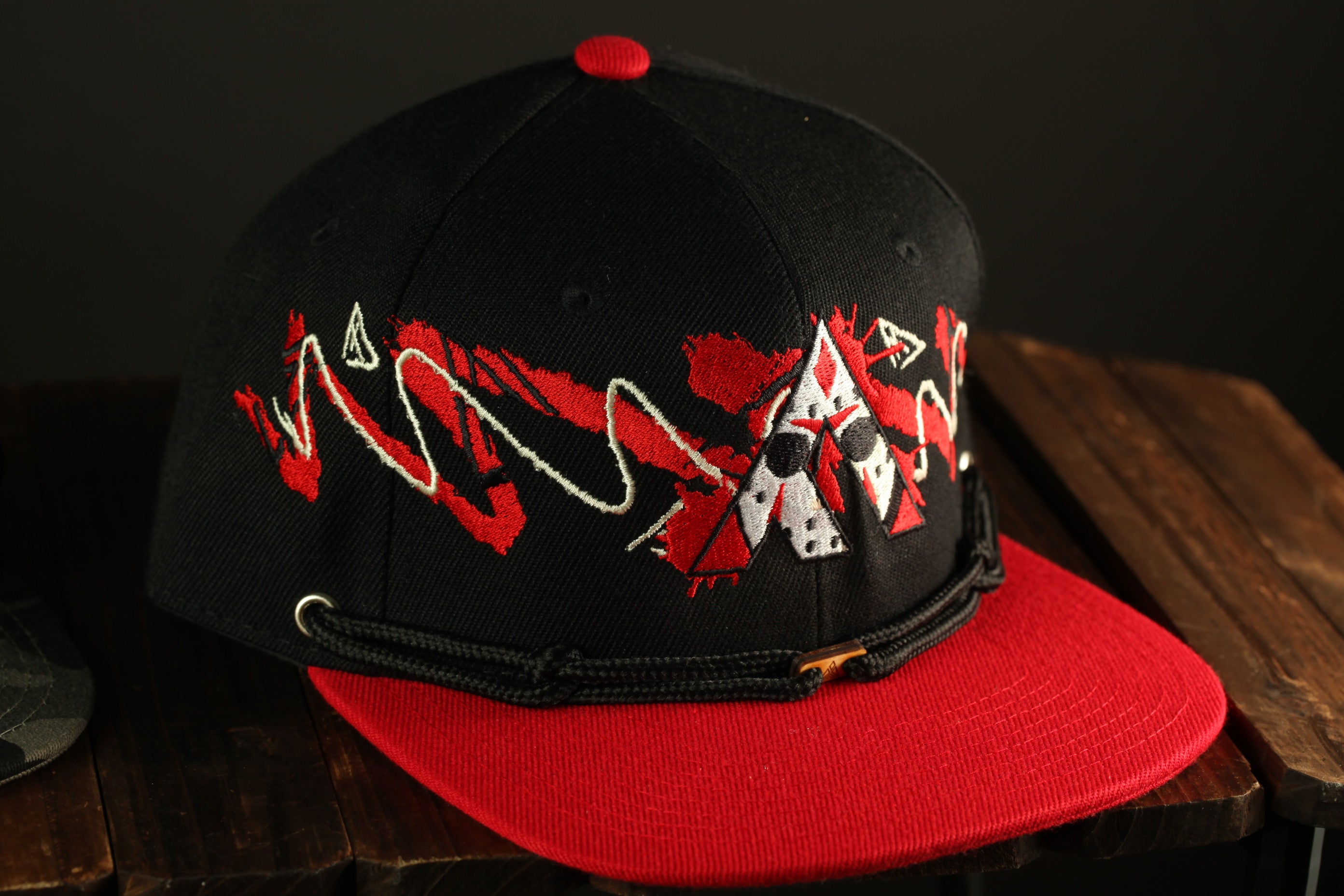 A black baseball cap with red trim and a graphic design on the front, placed on a wooden surface.