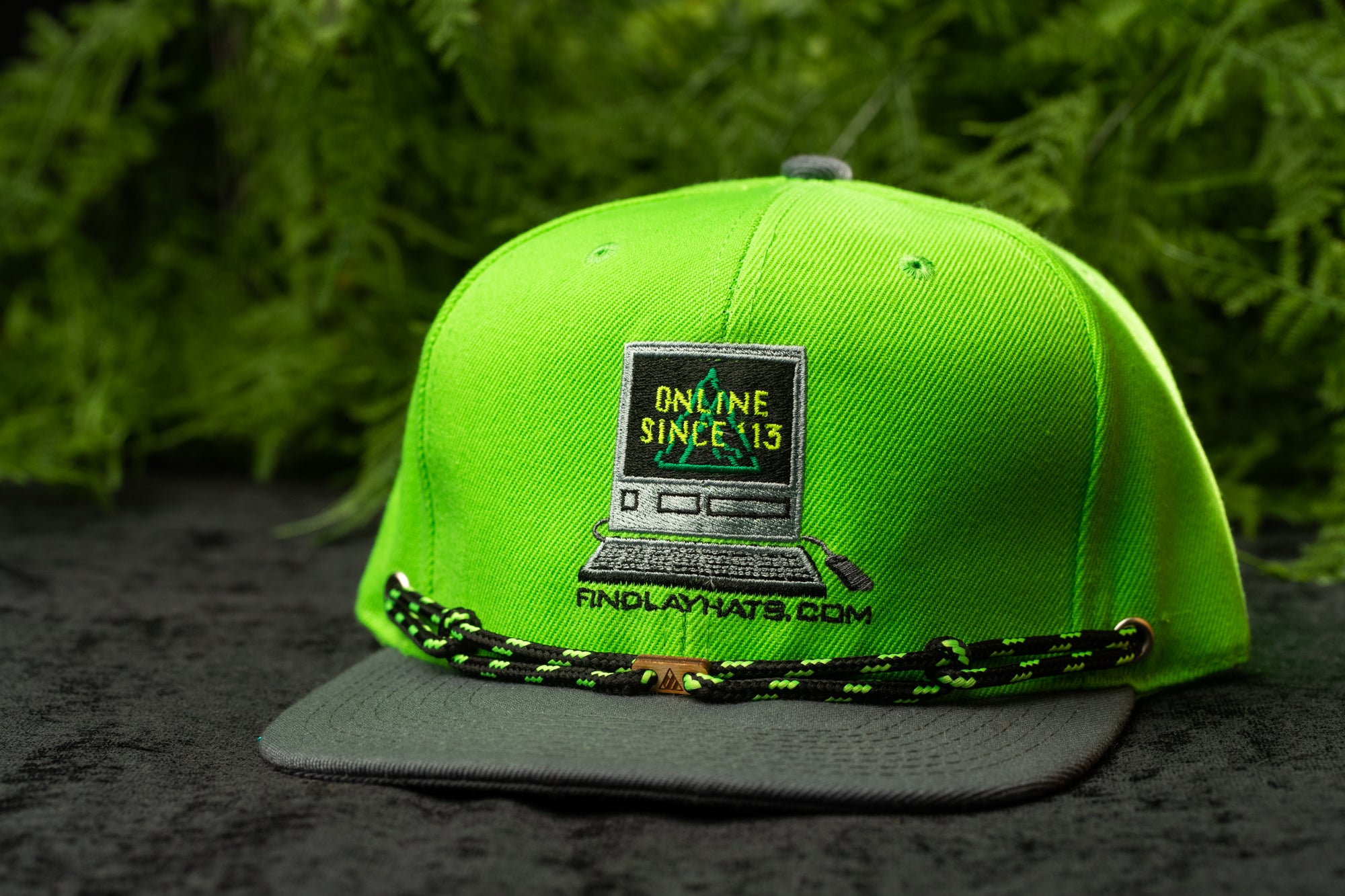 A neon green baseball cap with a graphic design on it, featuring a computer monitor and the text "Online Since 13" and "FINDLAYHATS.COM".