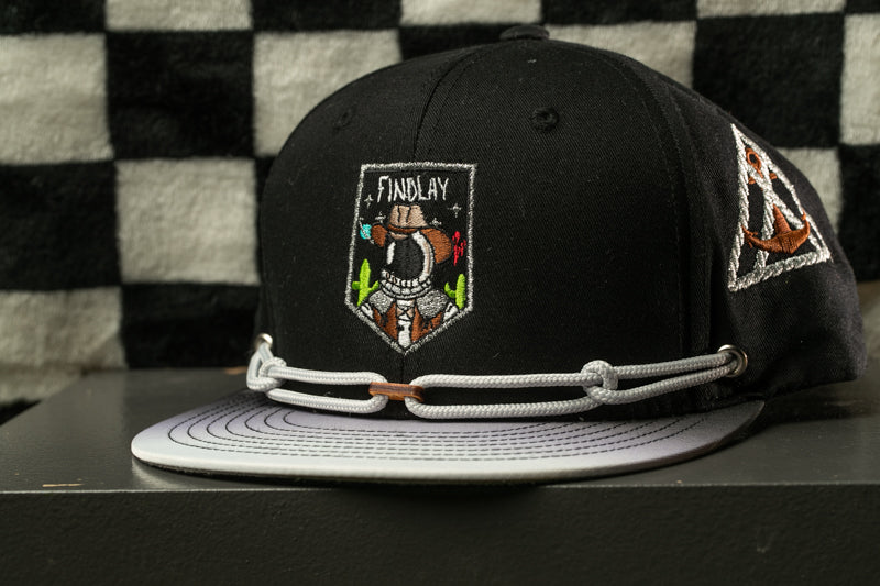 A black baseball cap with a white brim and a white band around the brim, featuring a patch with a cartoon character and the text "FINDLAY" on it.