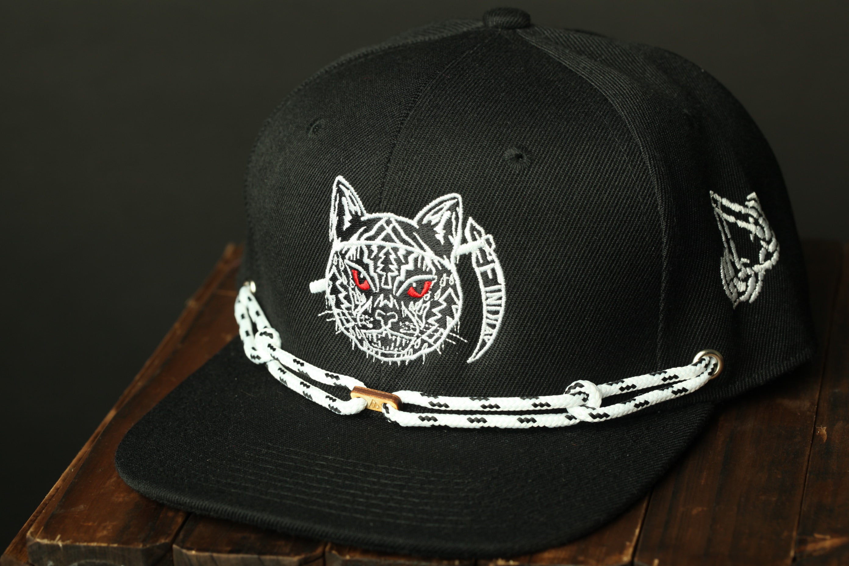 A black baseball cap with a white cat design and a chain strap.