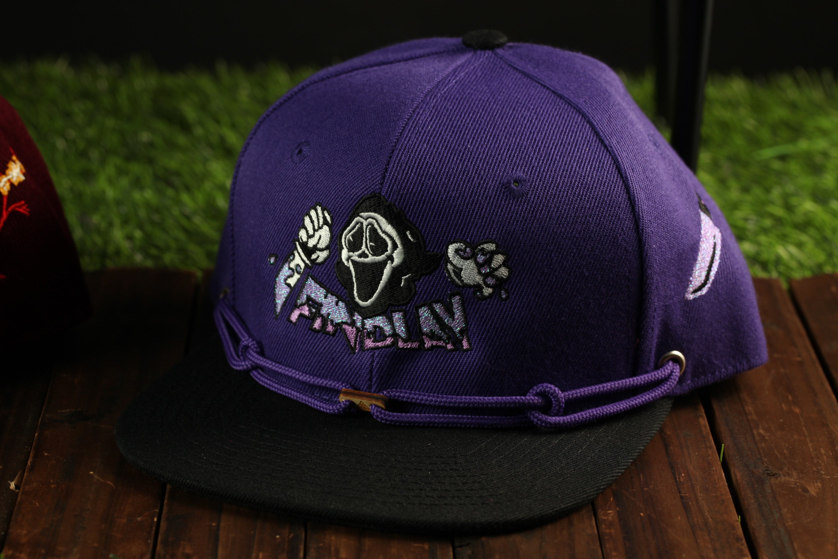 A purple baseball cap with a graphic design featuring a skull and the word "FINDLY" on it, sitting on a wooden surface.