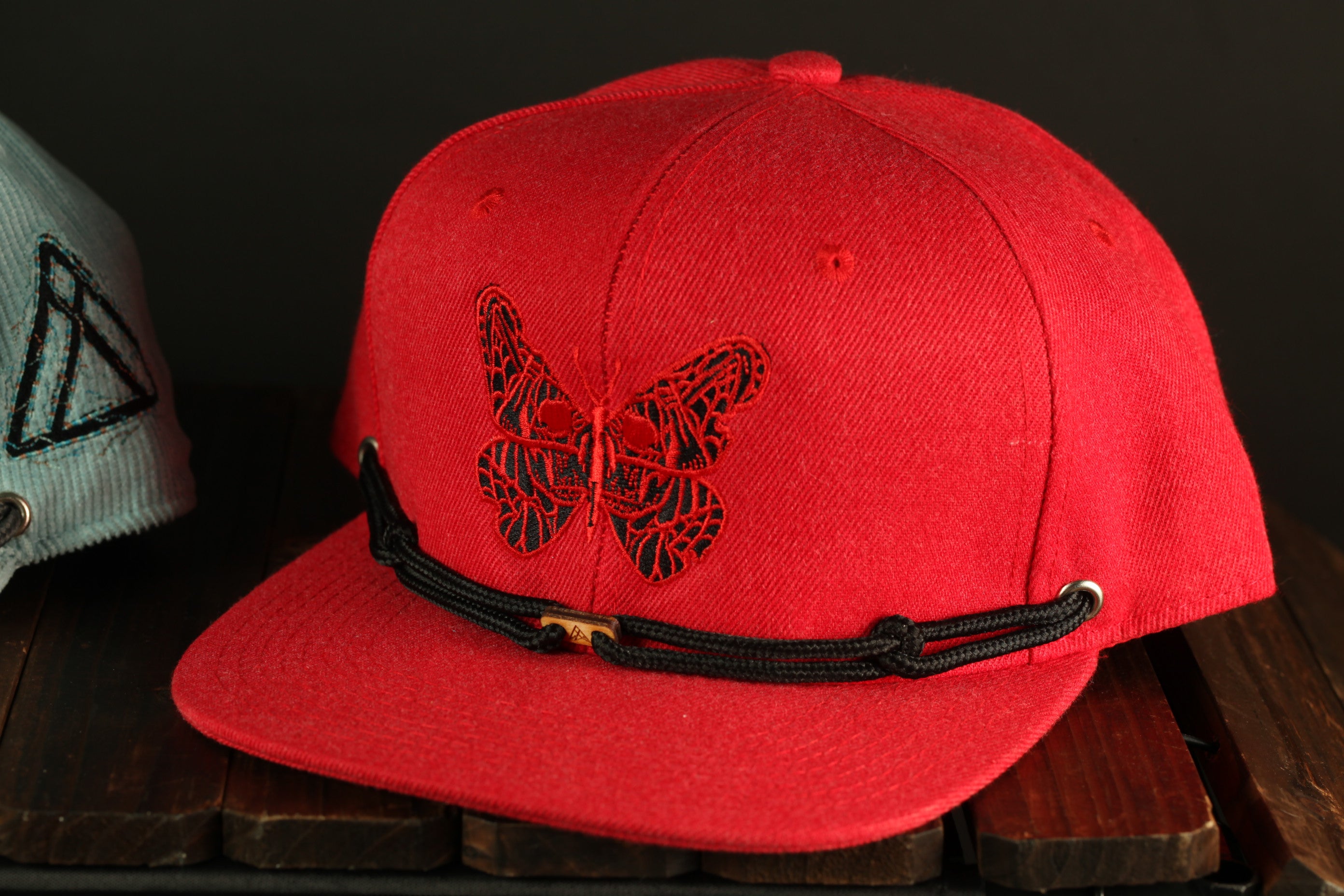A red baseball cap with a black butterfly embroidered on it, placed on a wooden surface.