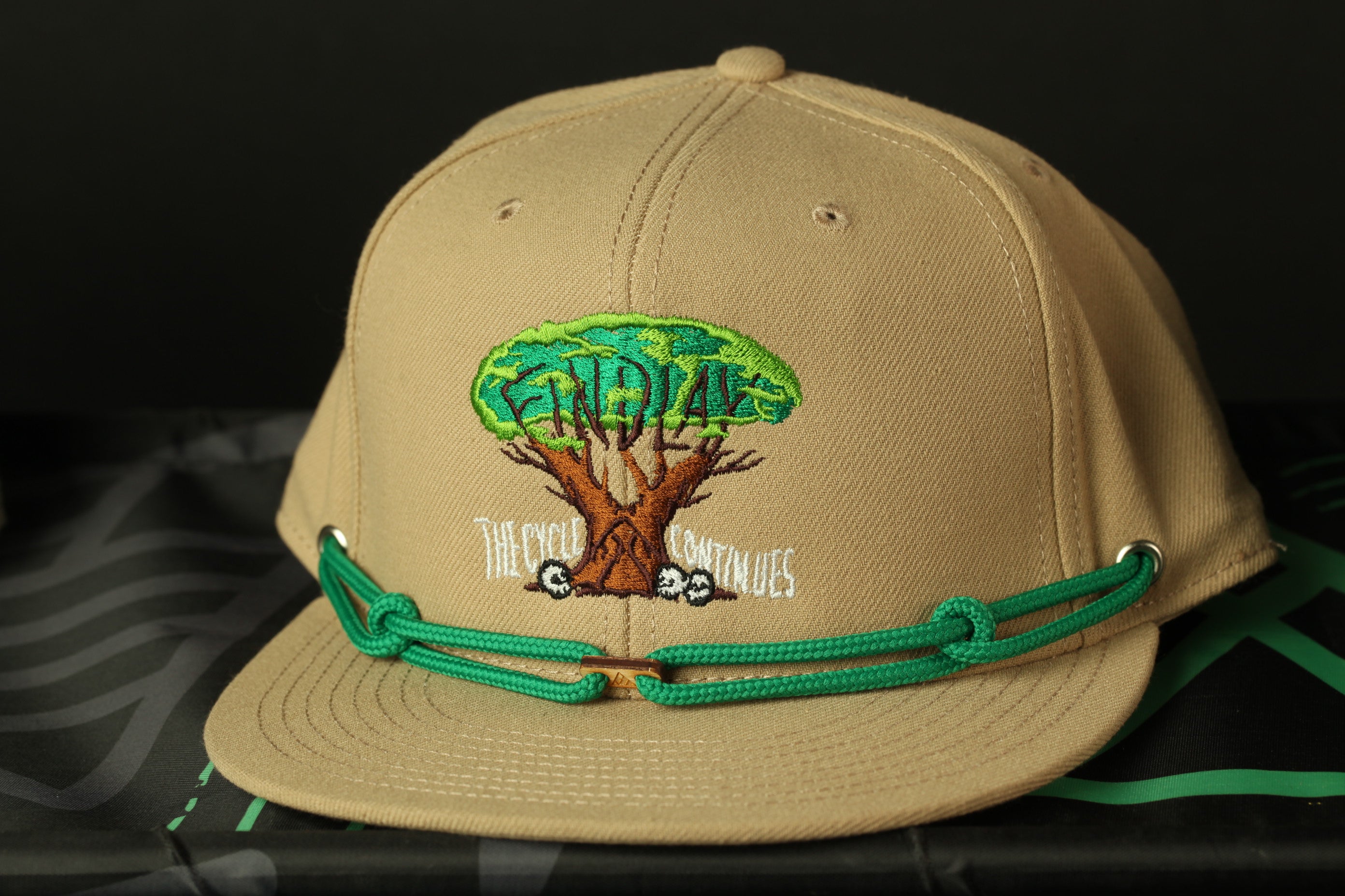 A beige baseball cap with a green string and a tree design on the front.