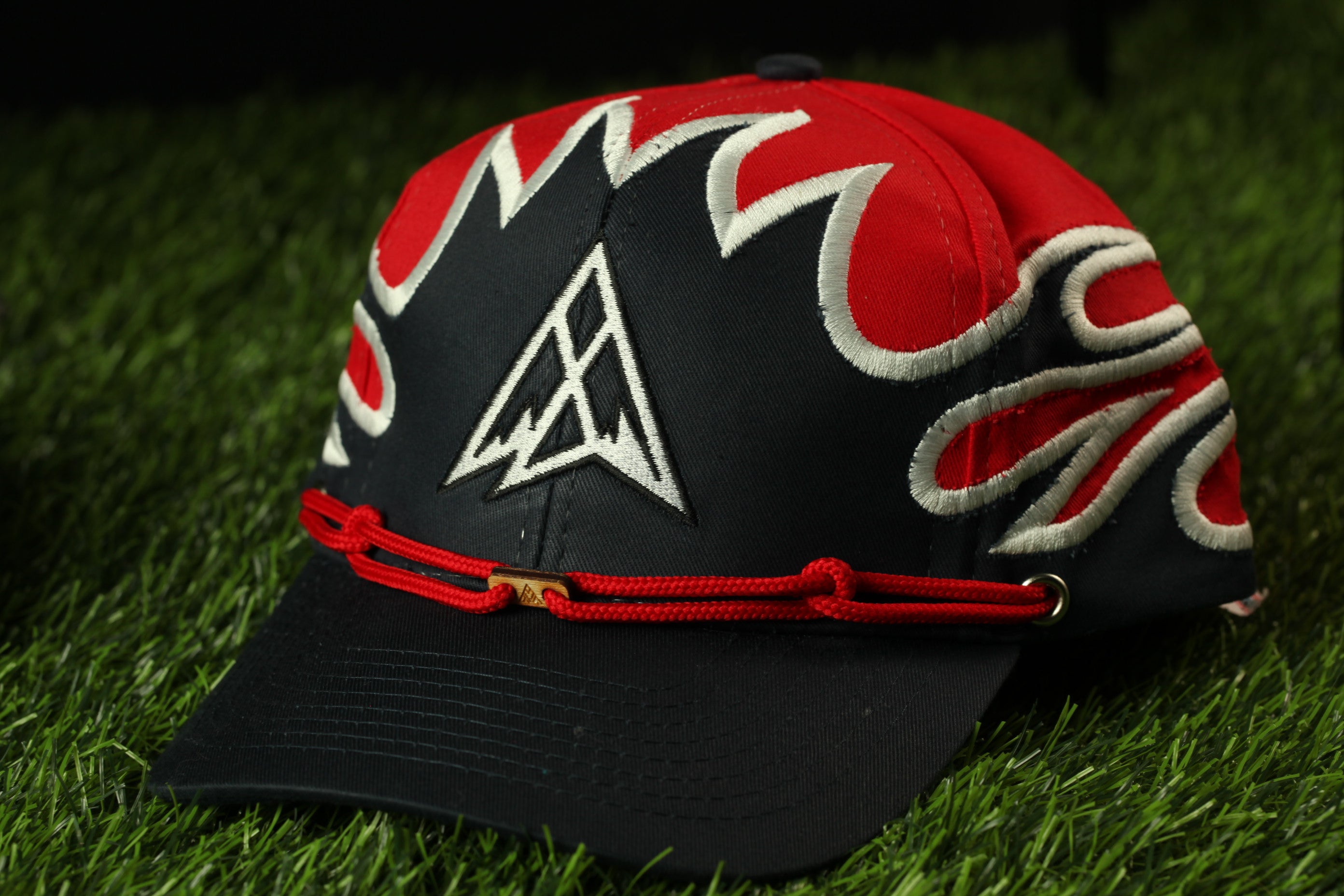 A red and black baseball cap with a white triangle logo on the front, resting on a grassy surface.