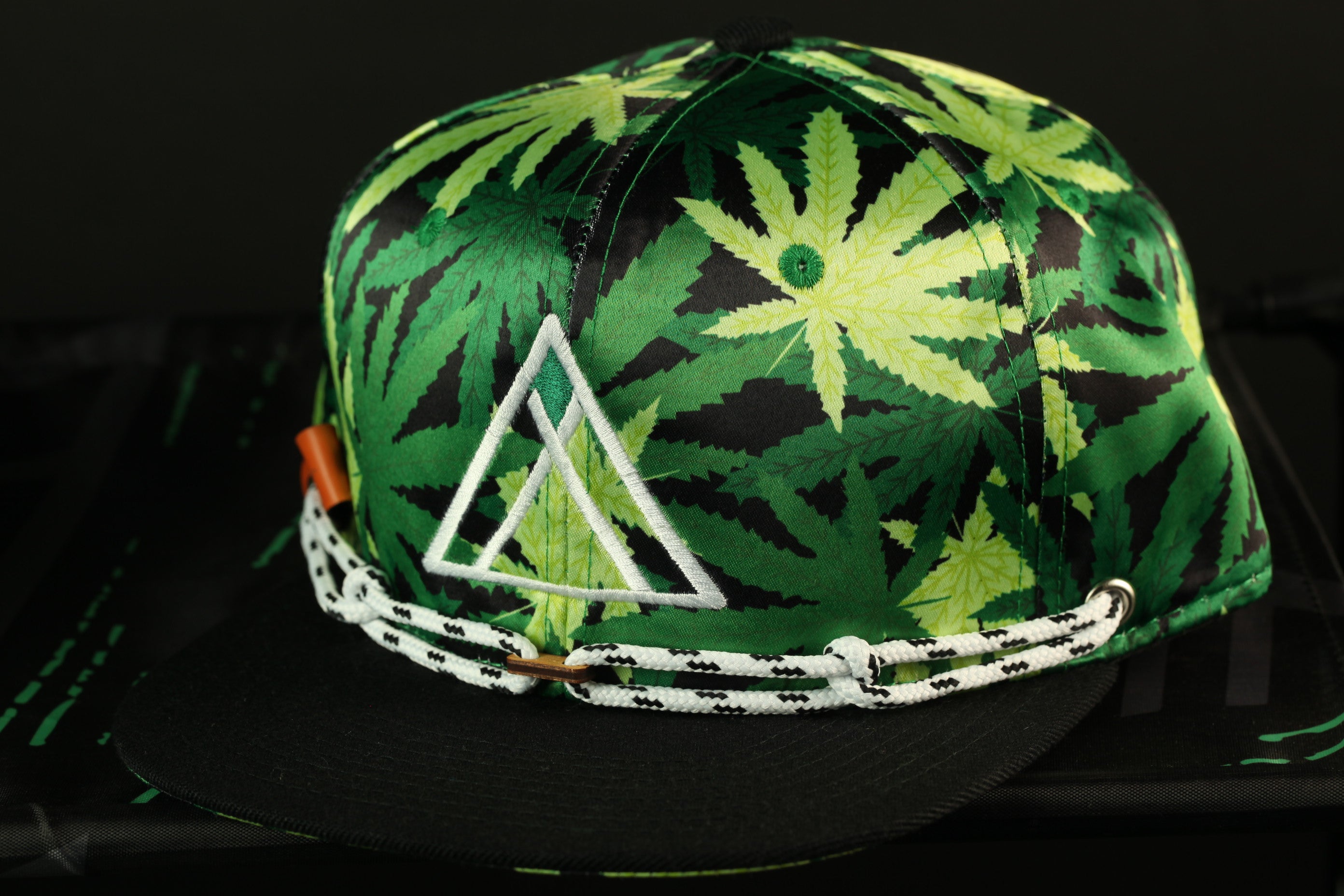 A green and black baseball cap with a leafy pattern and a white triangle logo on the front.