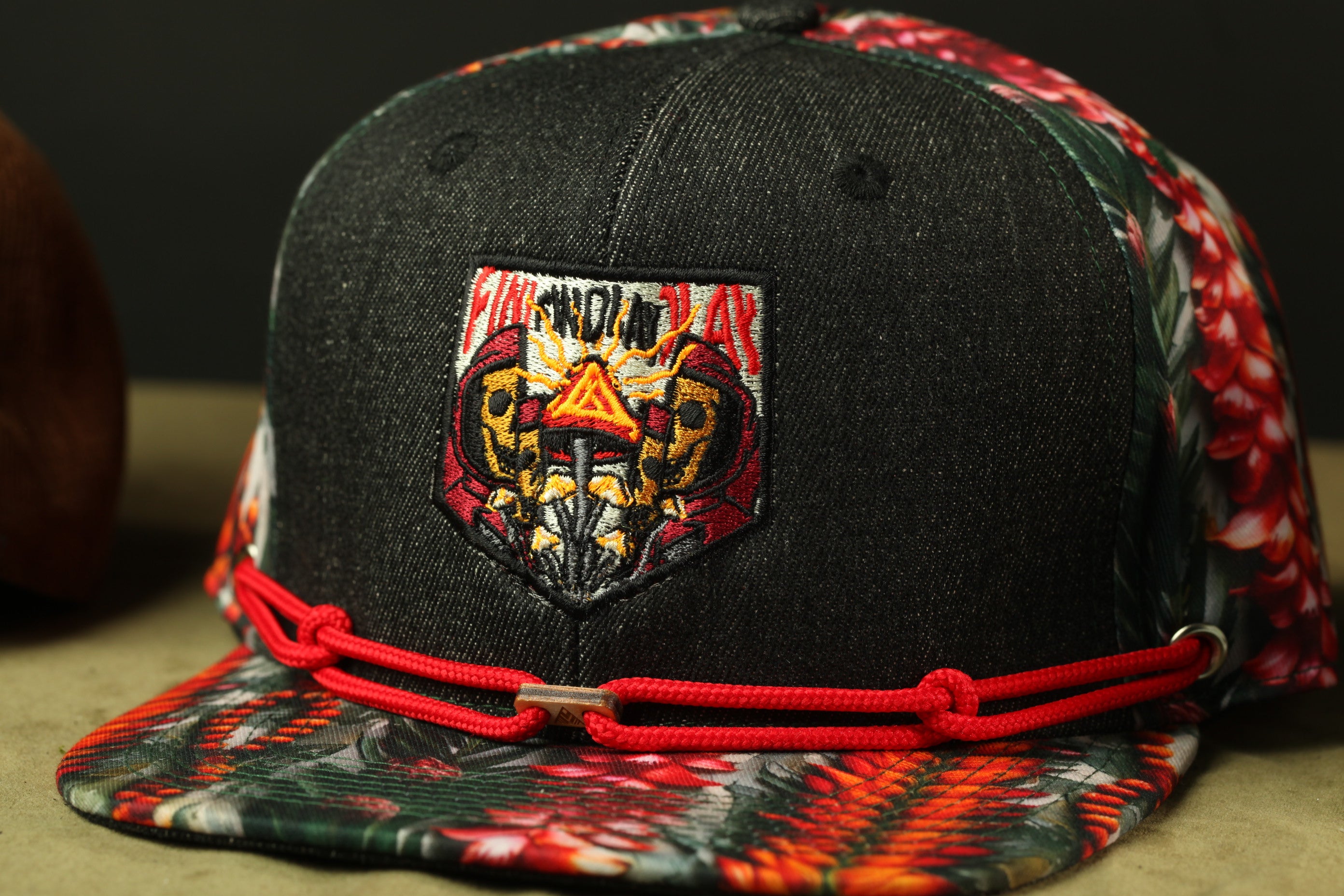 A black baseball cap with a colorful floral pattern and a red adjustable strap.