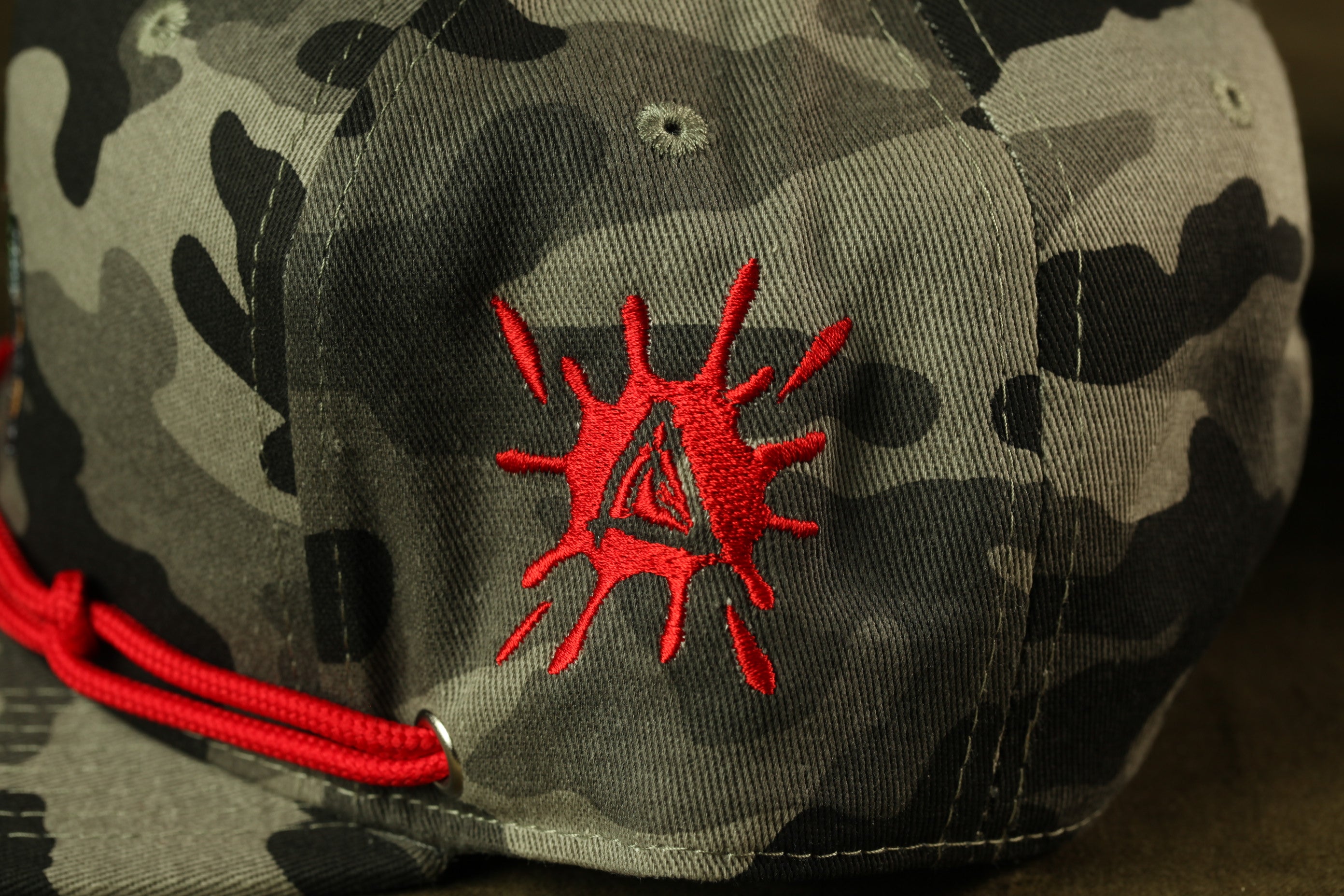 A close-up view of a camouflage baseball cap with a red triangle-shaped embroidered design on the front.