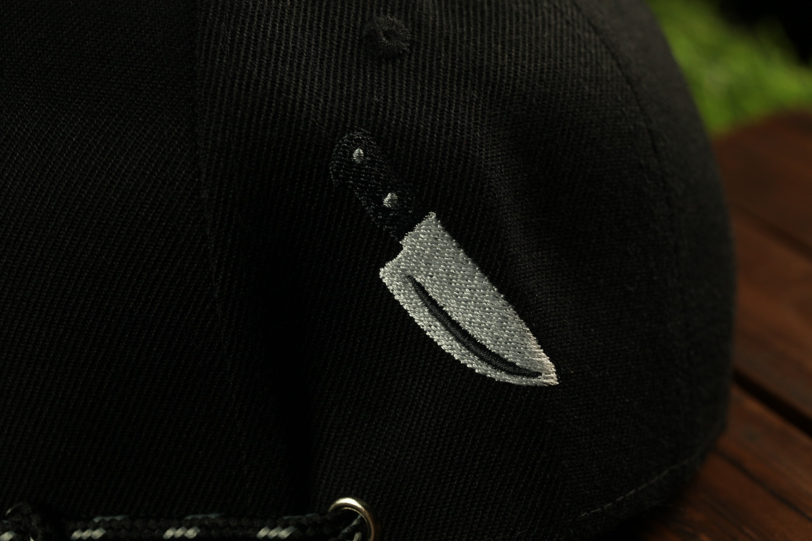 A close-up view of a black baseball cap with a white knife embroidered on the front.