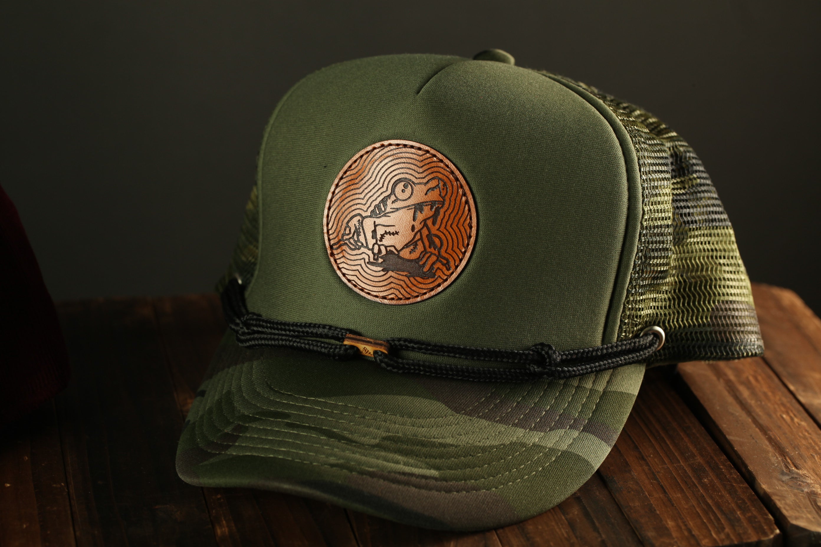 A green baseball cap with a circular logo featuring a frog design, resting on a wooden surface.