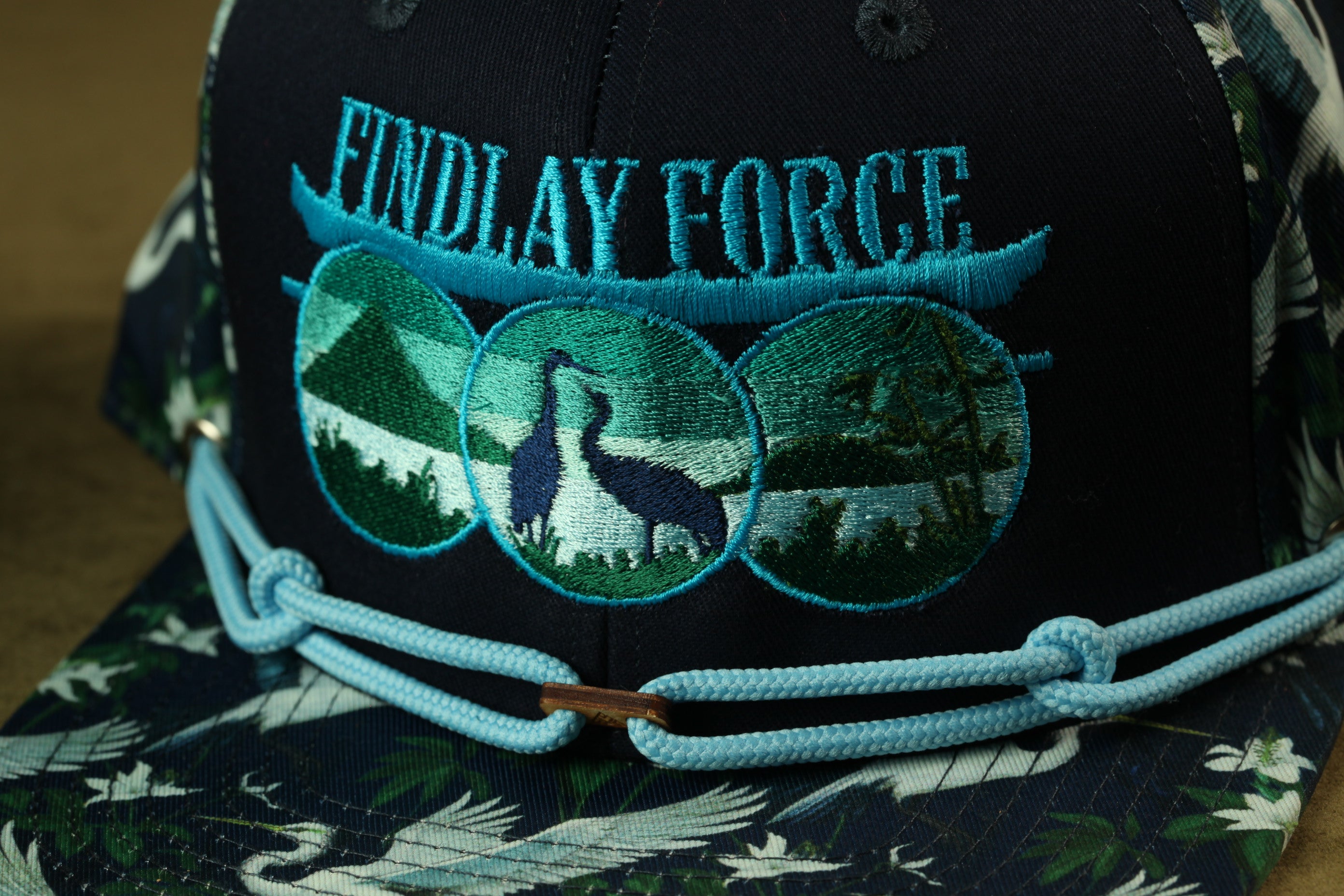 A close-up of a baseball cap with a floral pattern and a blue embroidered logo that says "Findlay Force".