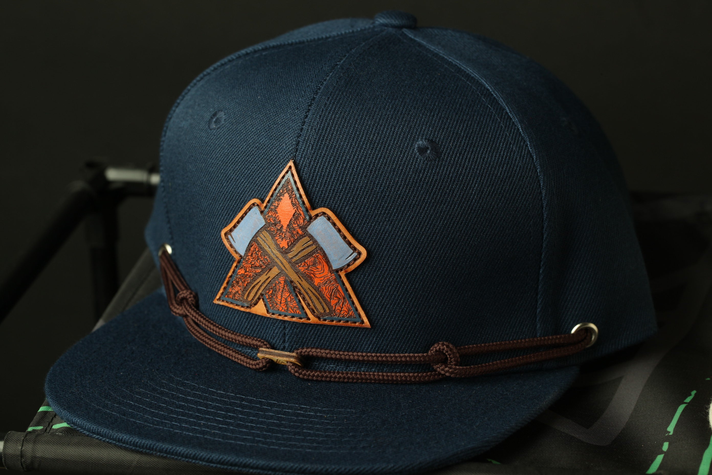 A navy blue baseball cap with a brown leather strap and a patch featuring an orange and brown design.