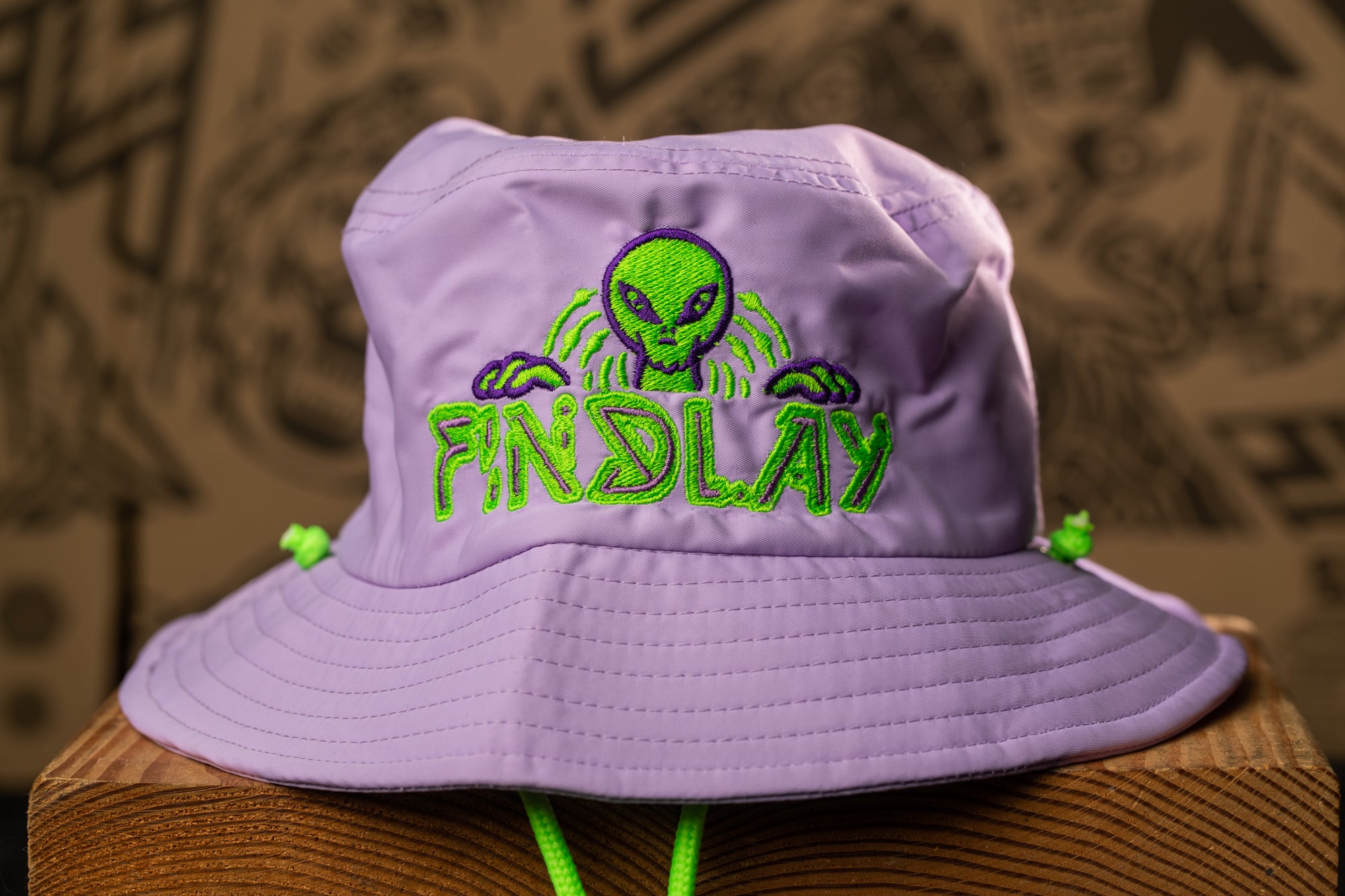 A purple bucket hat with a green alien design and the word "FINDlay" printed on it.