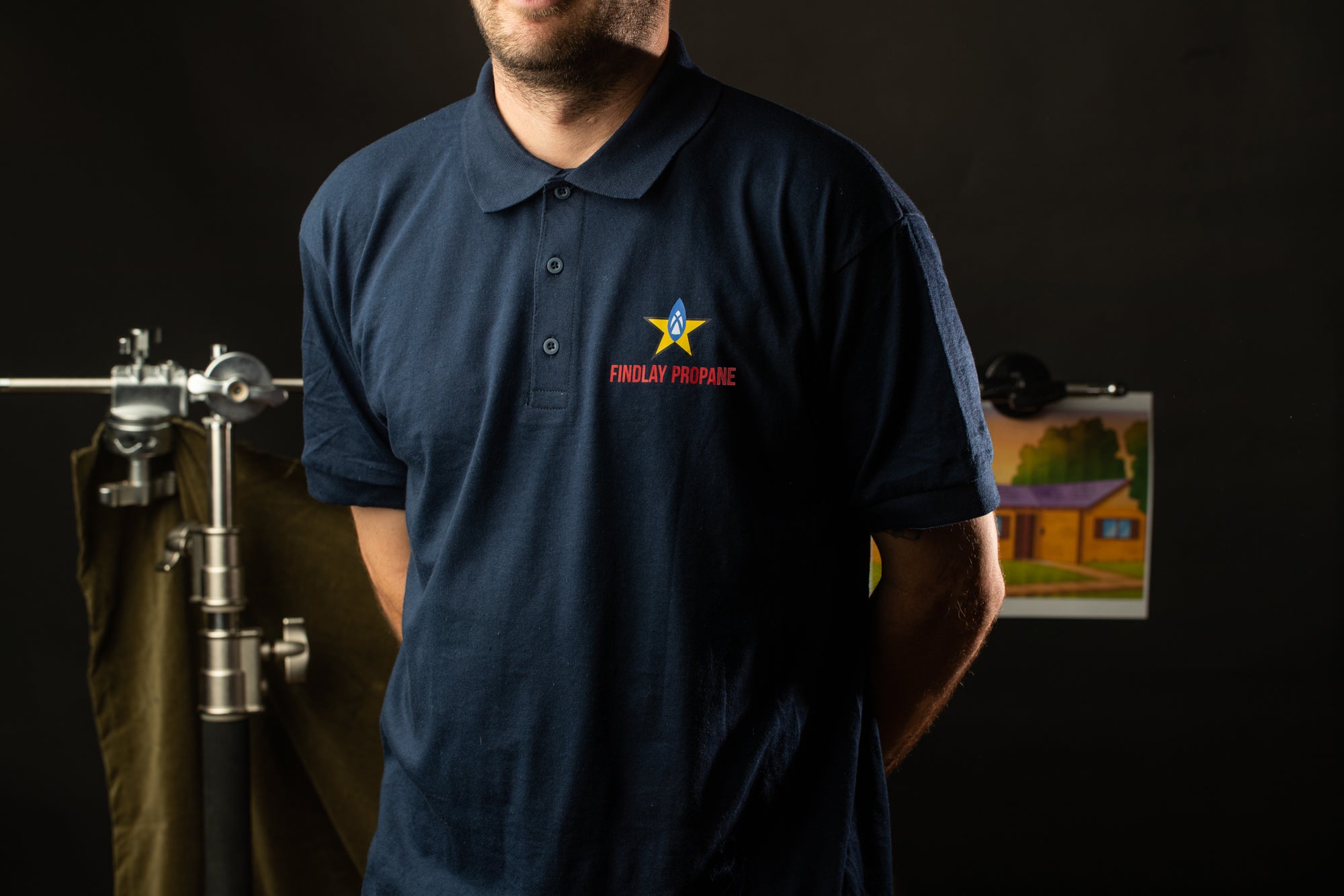 A man wearing a navy blue polo shirt with a logo stands in front of a dark background.