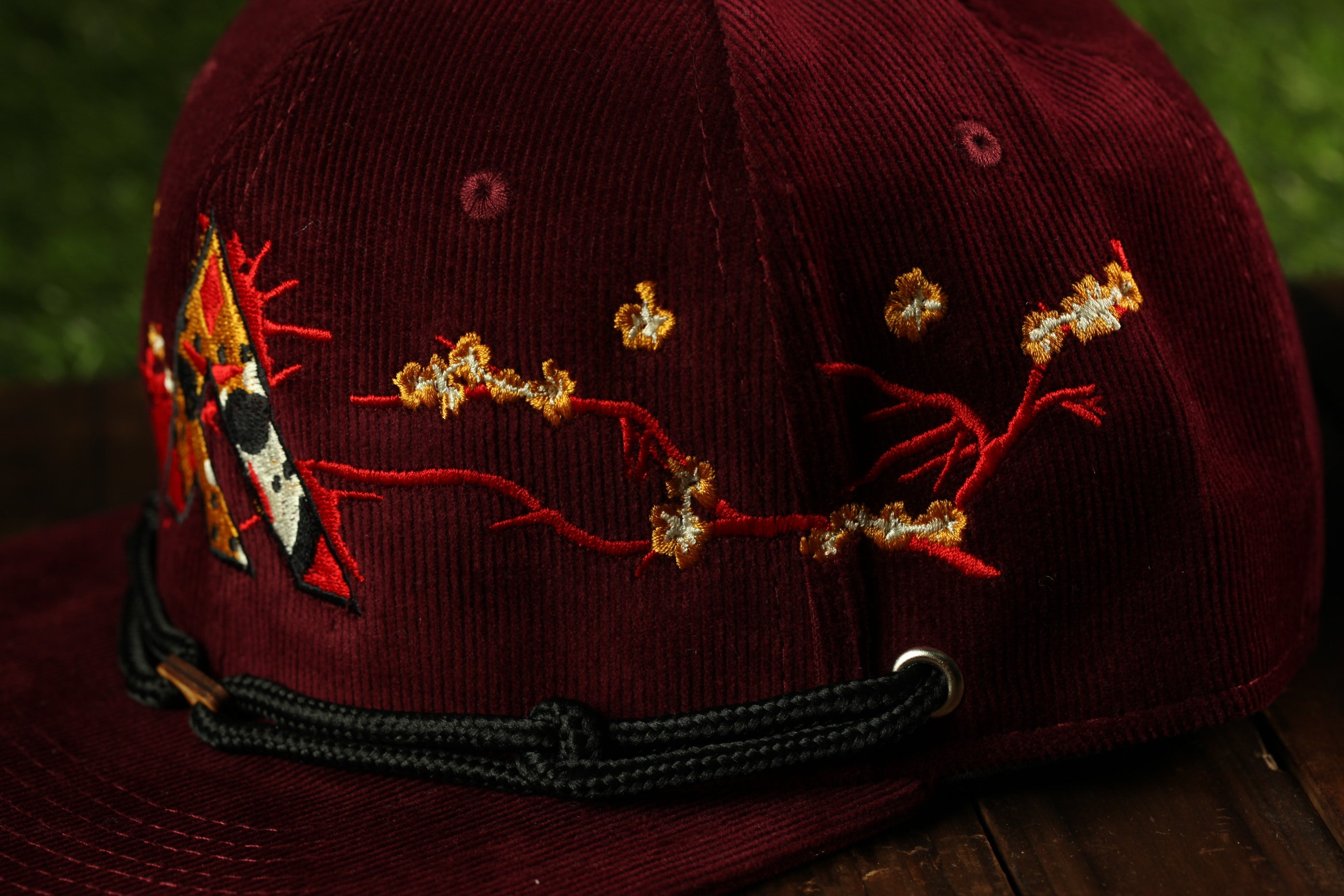 A close-up view of a burgundy baseball cap with a floral embroidered design on the front.