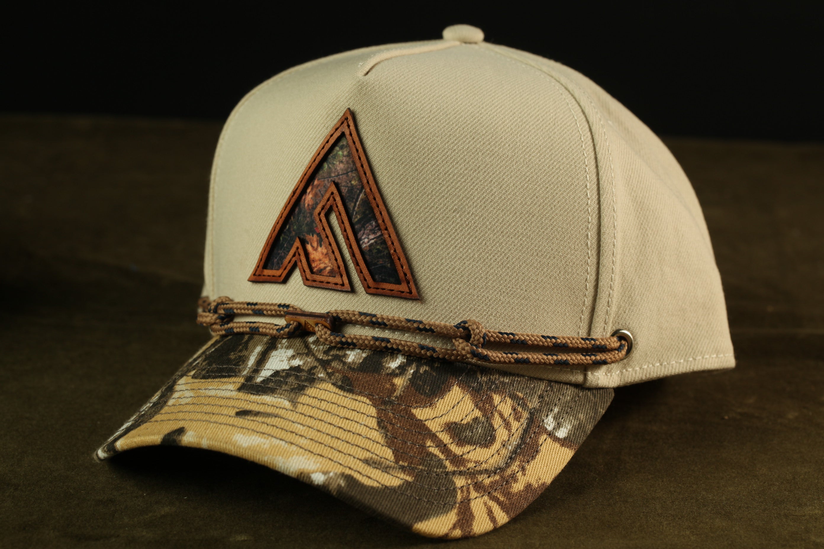 A beige baseball cap with a camouflage pattern and a logo on the front.