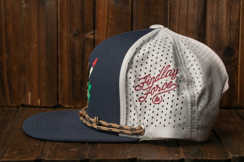 A navy blue baseball cap with a white perforated brim and a red logo on the side, placed on a wooden surface.