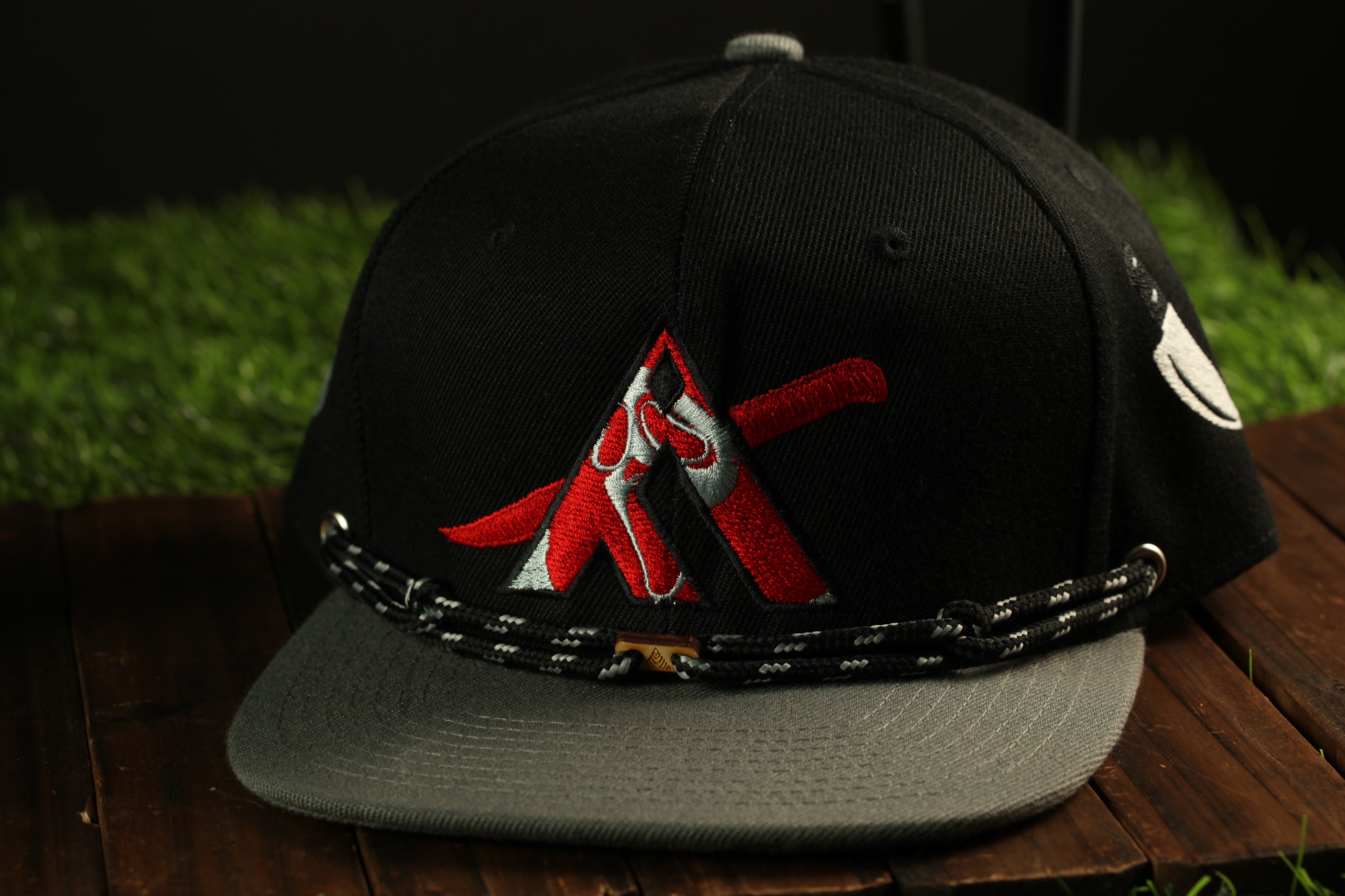 A black baseball cap with a red and white logo on the front, sitting on a wooden surface.