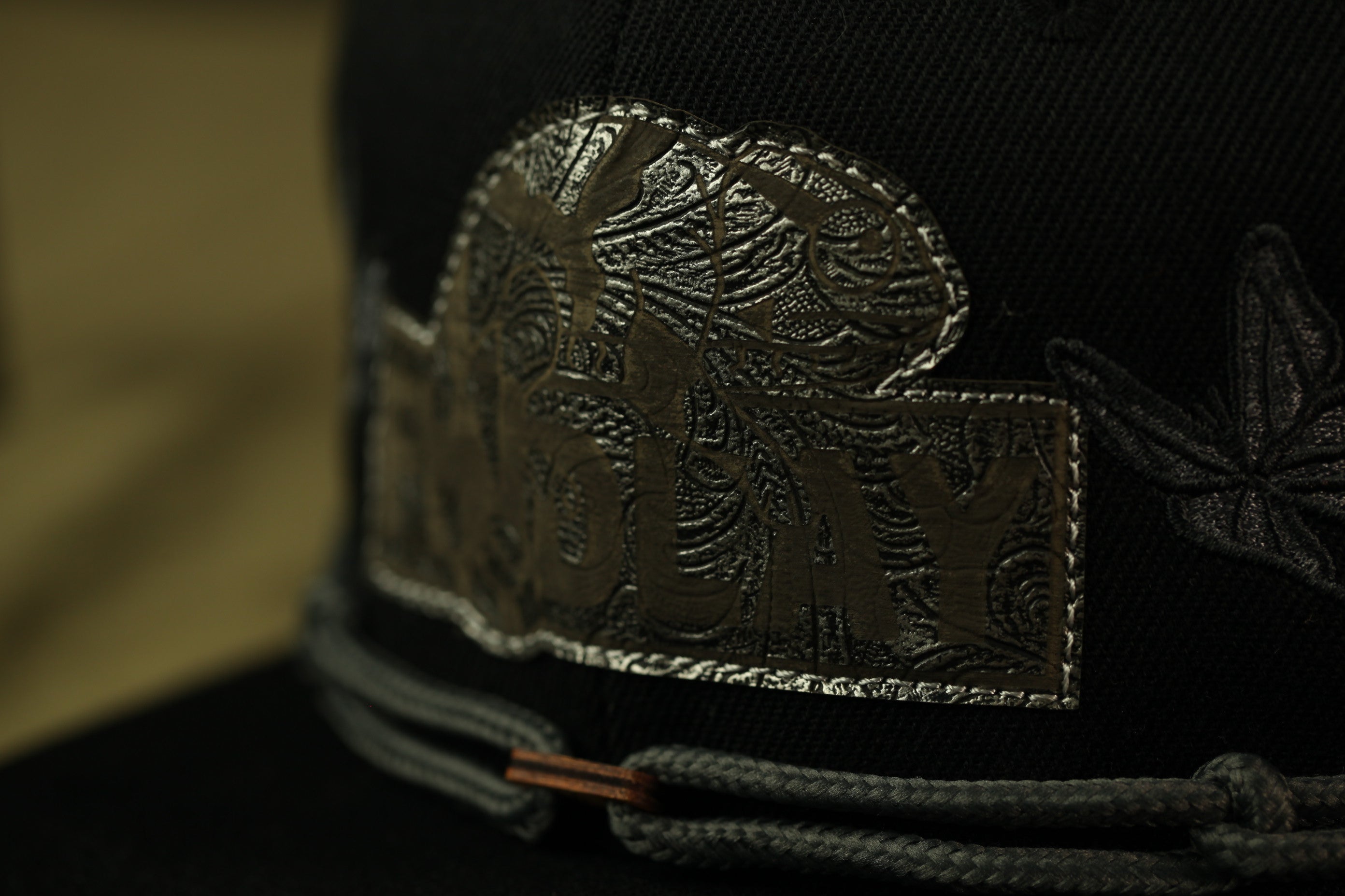 A close-up view of a black baseball cap with a decorative metal logo on the front.