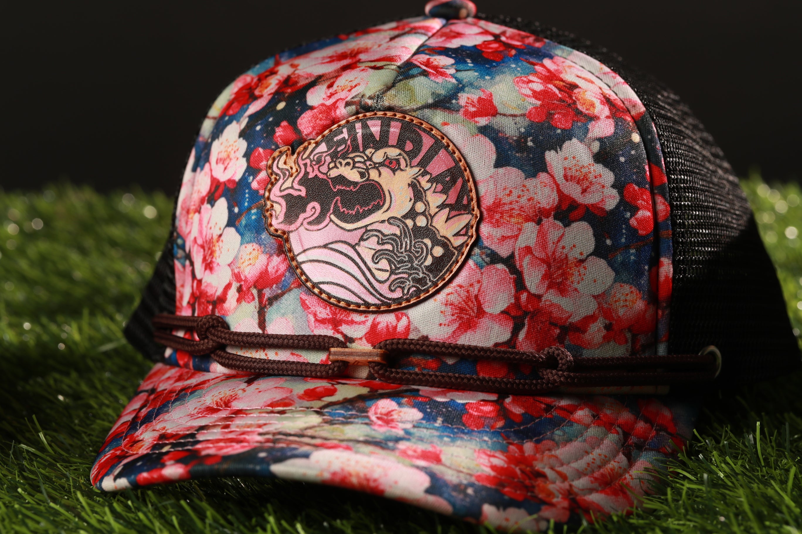 A colorful floral-patterned baseball cap with a dragon design on the front, resting on a grassy surface.