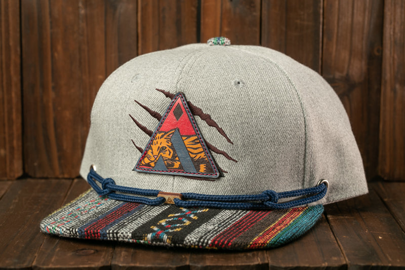 A gray baseball cap with a colorful, patterned brim and a patch featuring a tiger design, placed on a wooden surface.