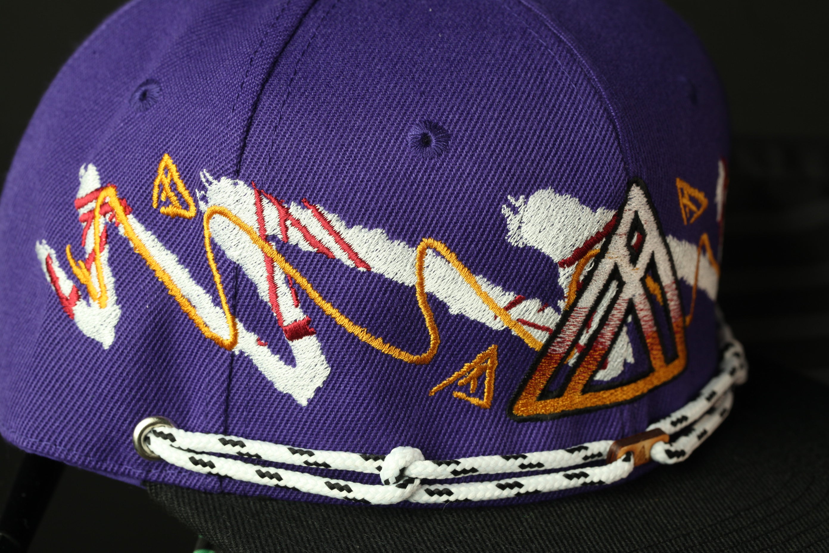 A close-up view of a purple baseball cap with a unique, colorful design featuring a zigzag pattern and a triangle-shaped element.