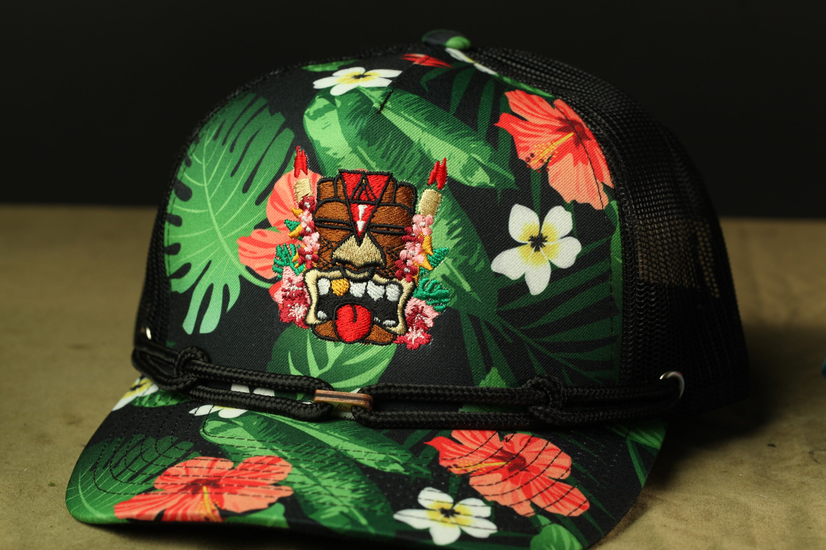 A colorful baseball cap with a tropical flower pattern, including hibiscus and other flowers, and a tiki mask design.