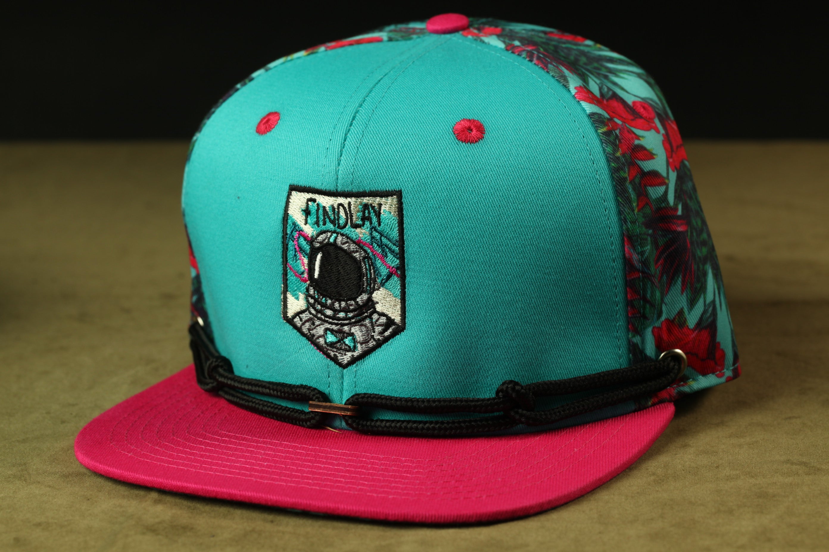 A turquoise baseball cap with a floral pattern and a small patch on the front displaying the word "INDOLAY".