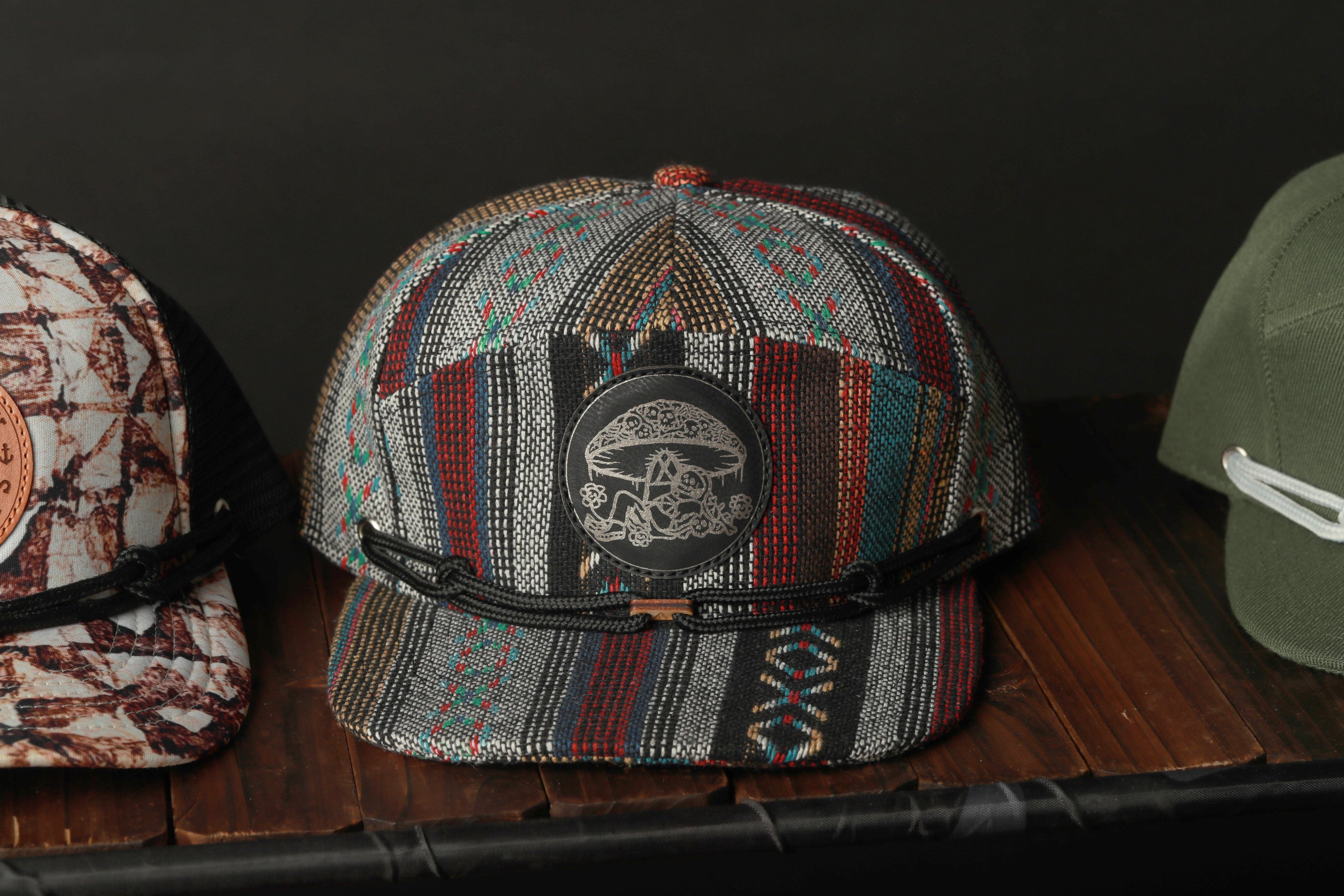 A colorful, patterned baseball cap with a unique design sits on a wooden surface, surrounded by other hats.