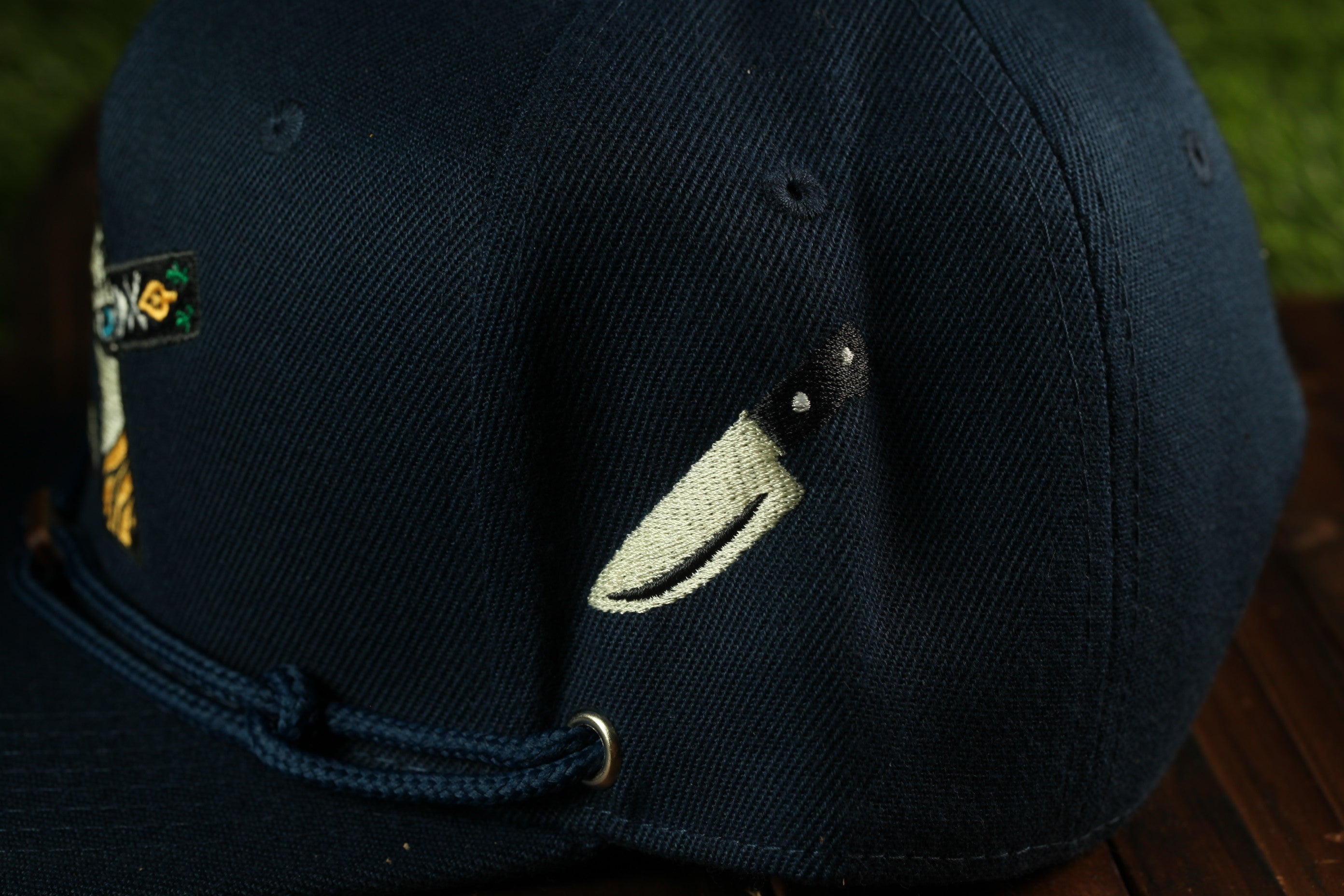 A close-up view of a dark blue baseball cap with a knife embroidered on the side.