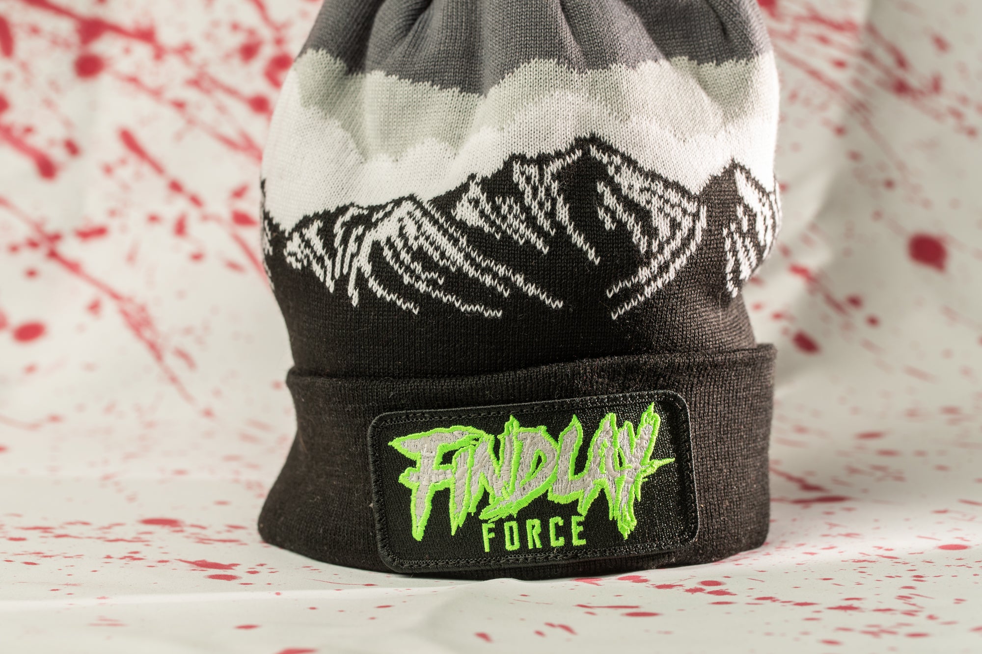 A black and gray beanie with a white mountain design and a green patch on the front that says "FINDlay Force".