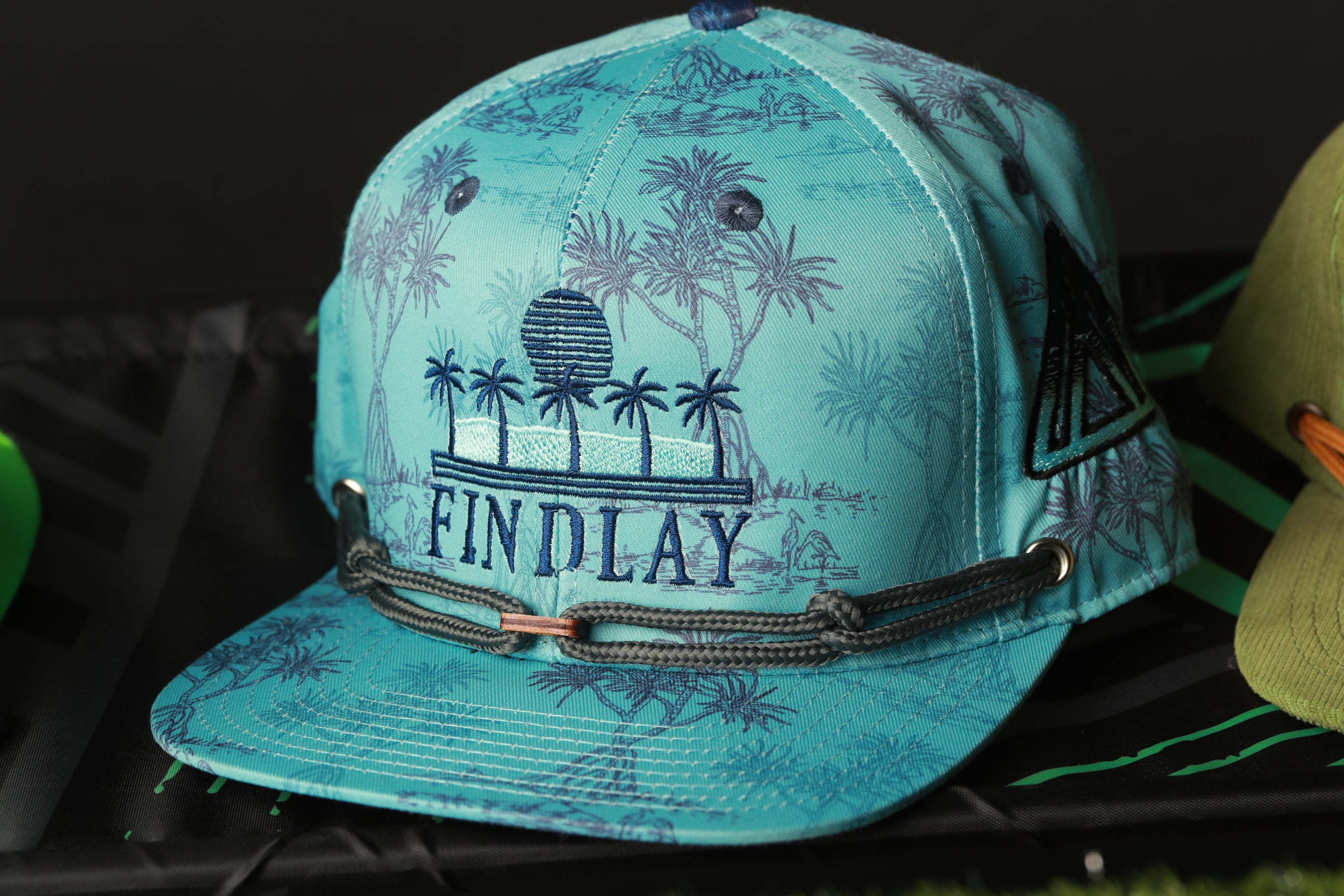 A turquoise baseball cap with a tropical print design and the word "FINDLAY" printed on it.
