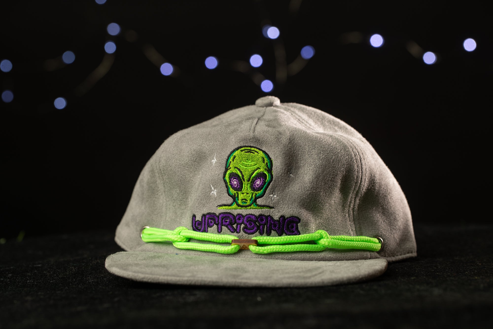 A gray baseball cap with a green alien design and the word "WIPRIS" printed on it, set against a dark background with twinkling lights.