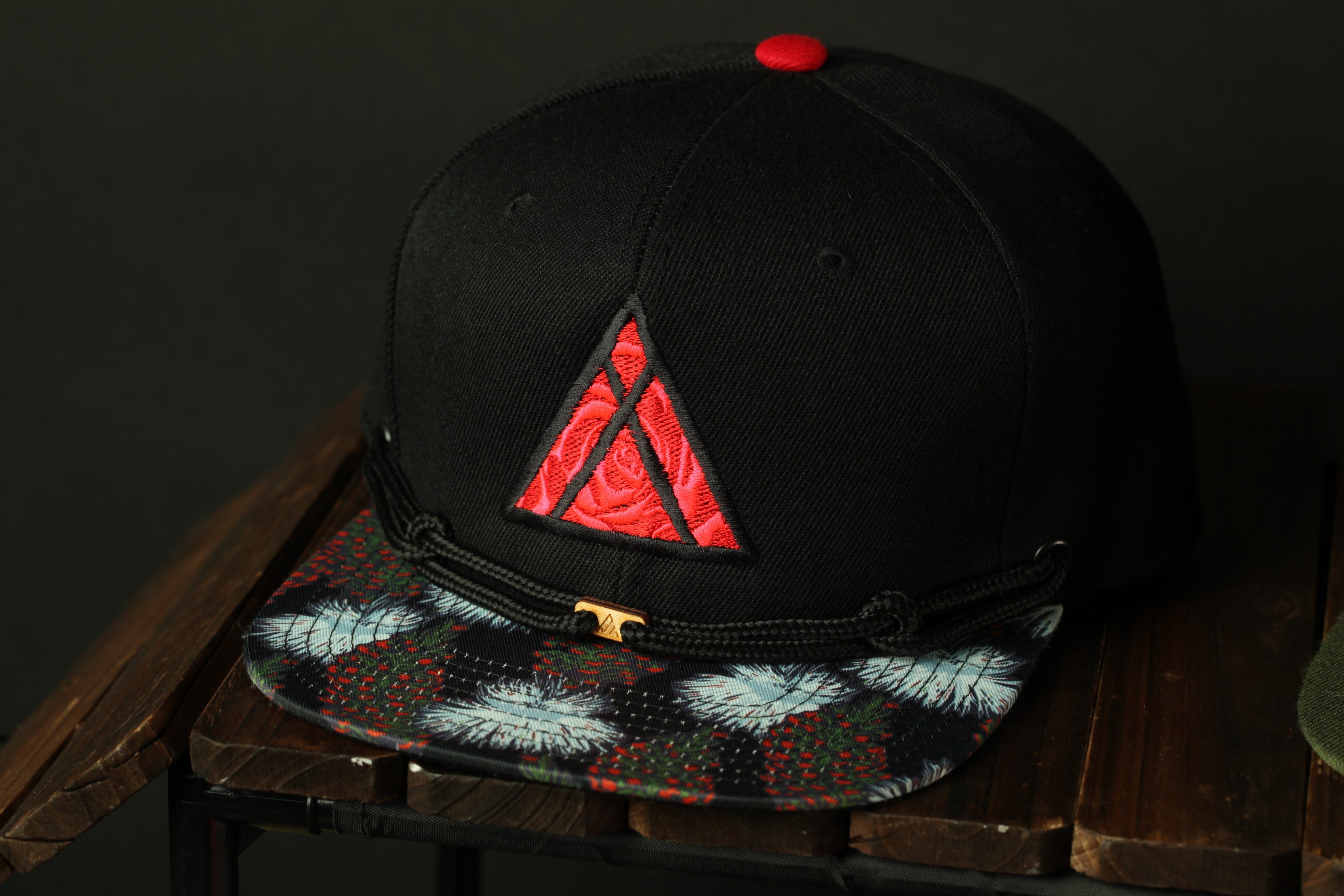 A black baseball cap with a red triangle design on the front, placed on a wooden surface.