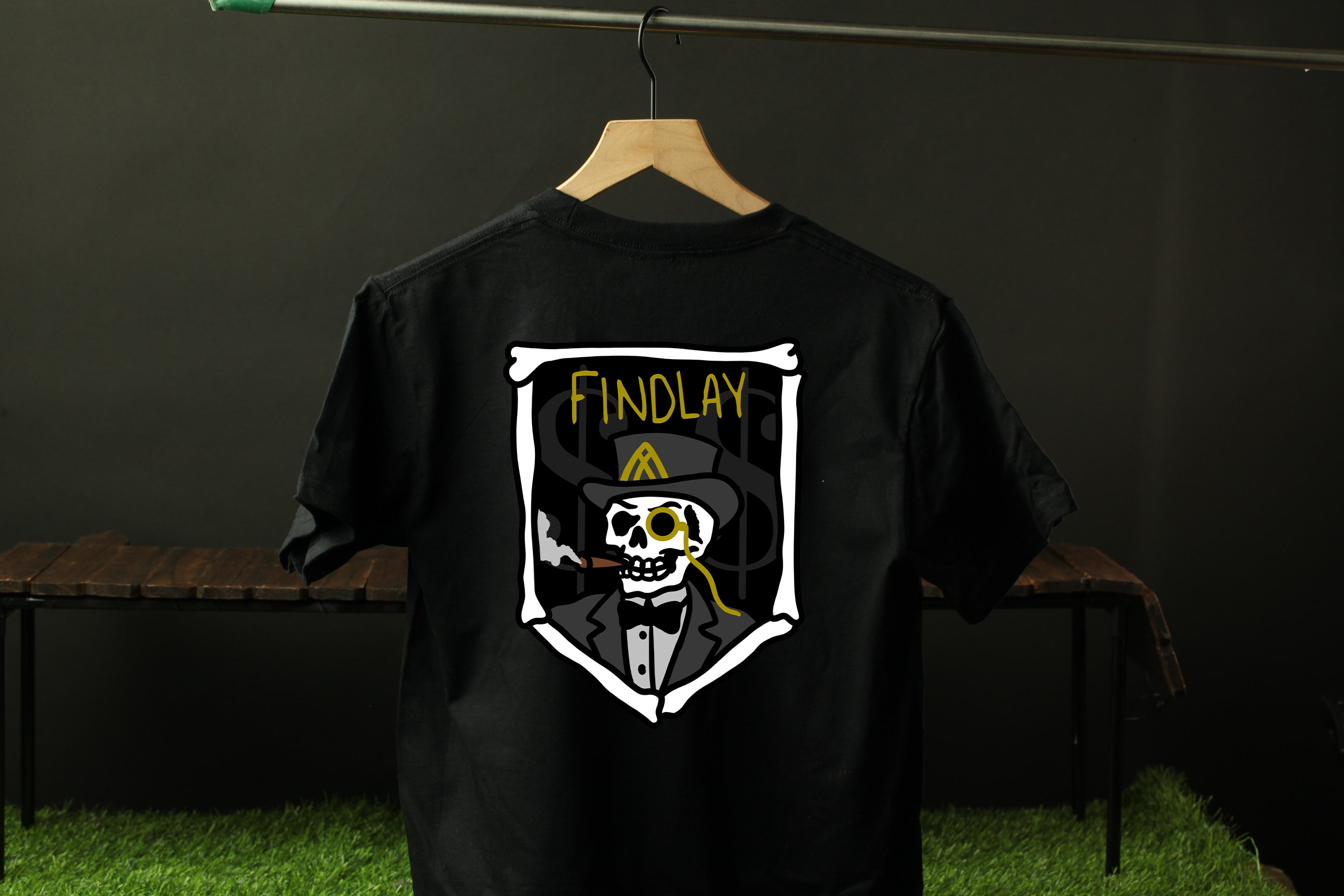 A black t-shirt with a graphic design featuring a skull wearing a top hat and a coat, with the text "FINDLAY" displayed on the shirt.