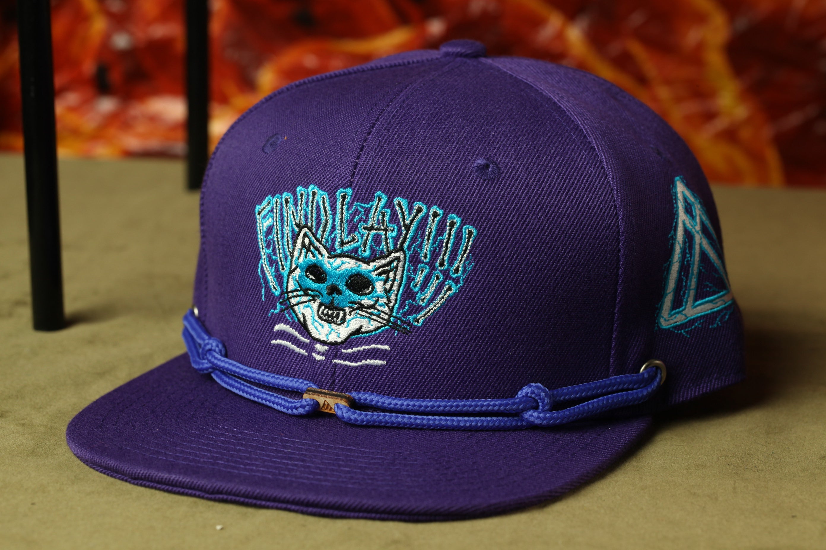 A purple baseball cap with a cat design and a blue strap.