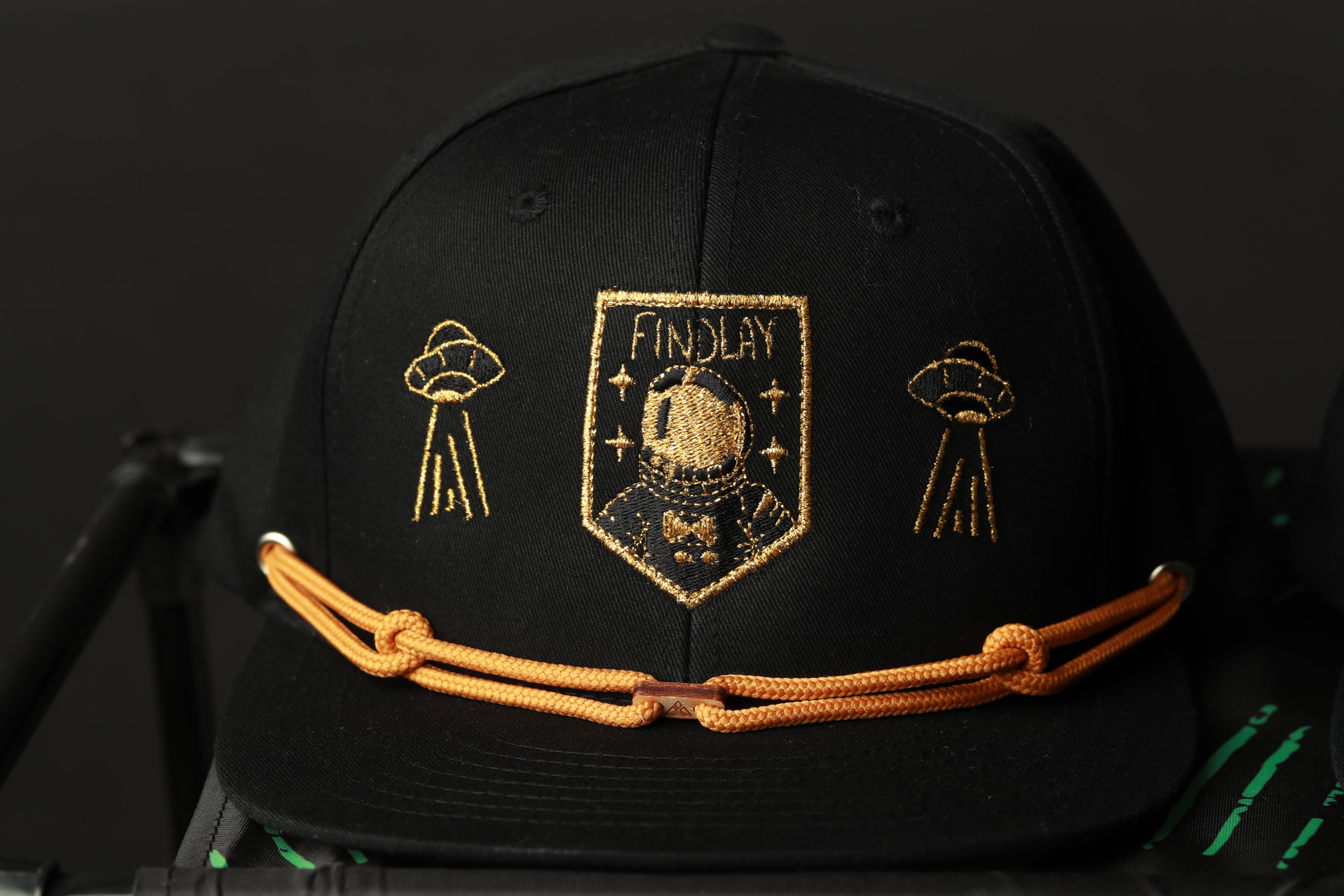 A black baseball cap with gold embroidered designs and text.
