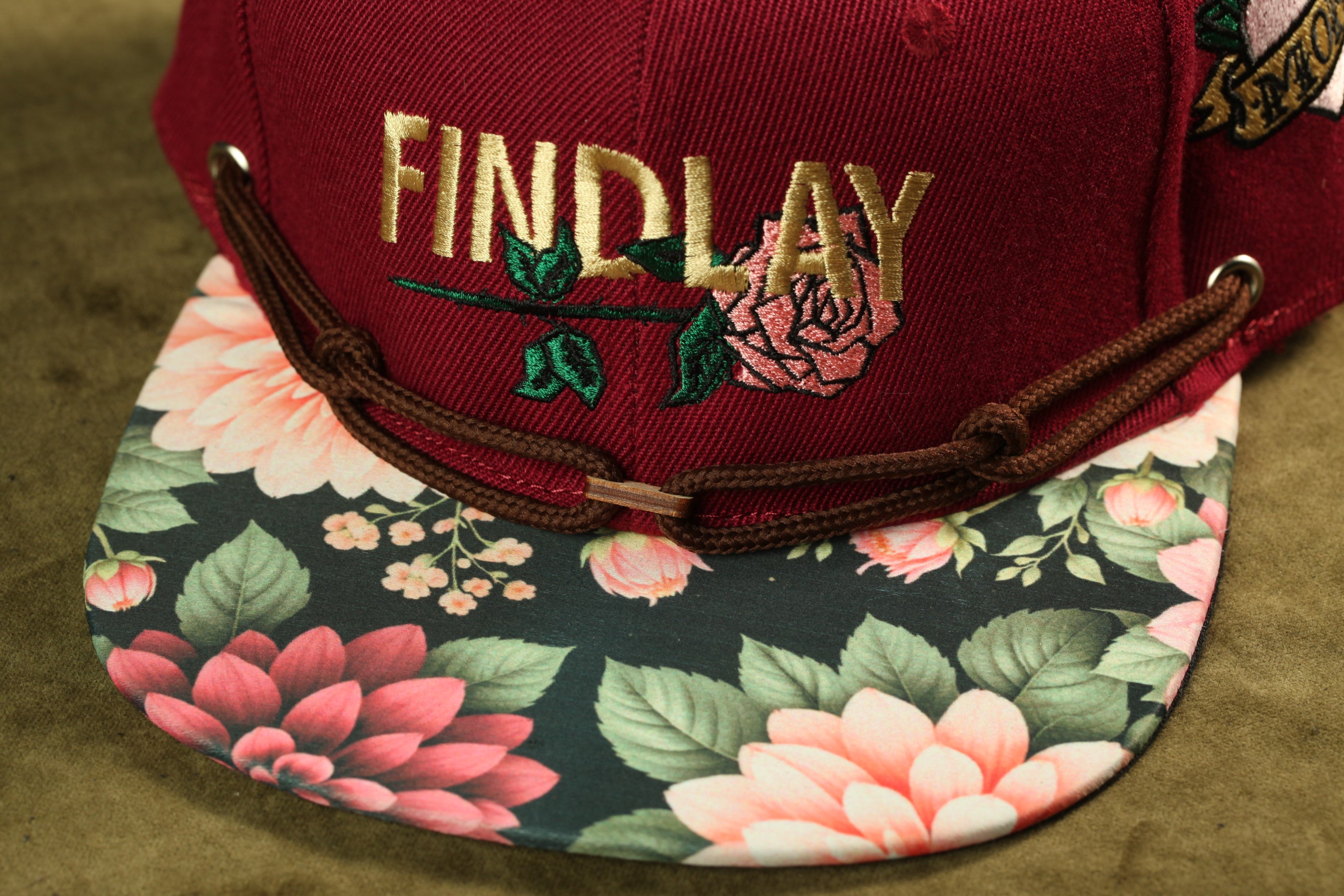 A close-up image of a burgundy baseball cap with a floral pattern and the word "FINDlay" embroidered on it.