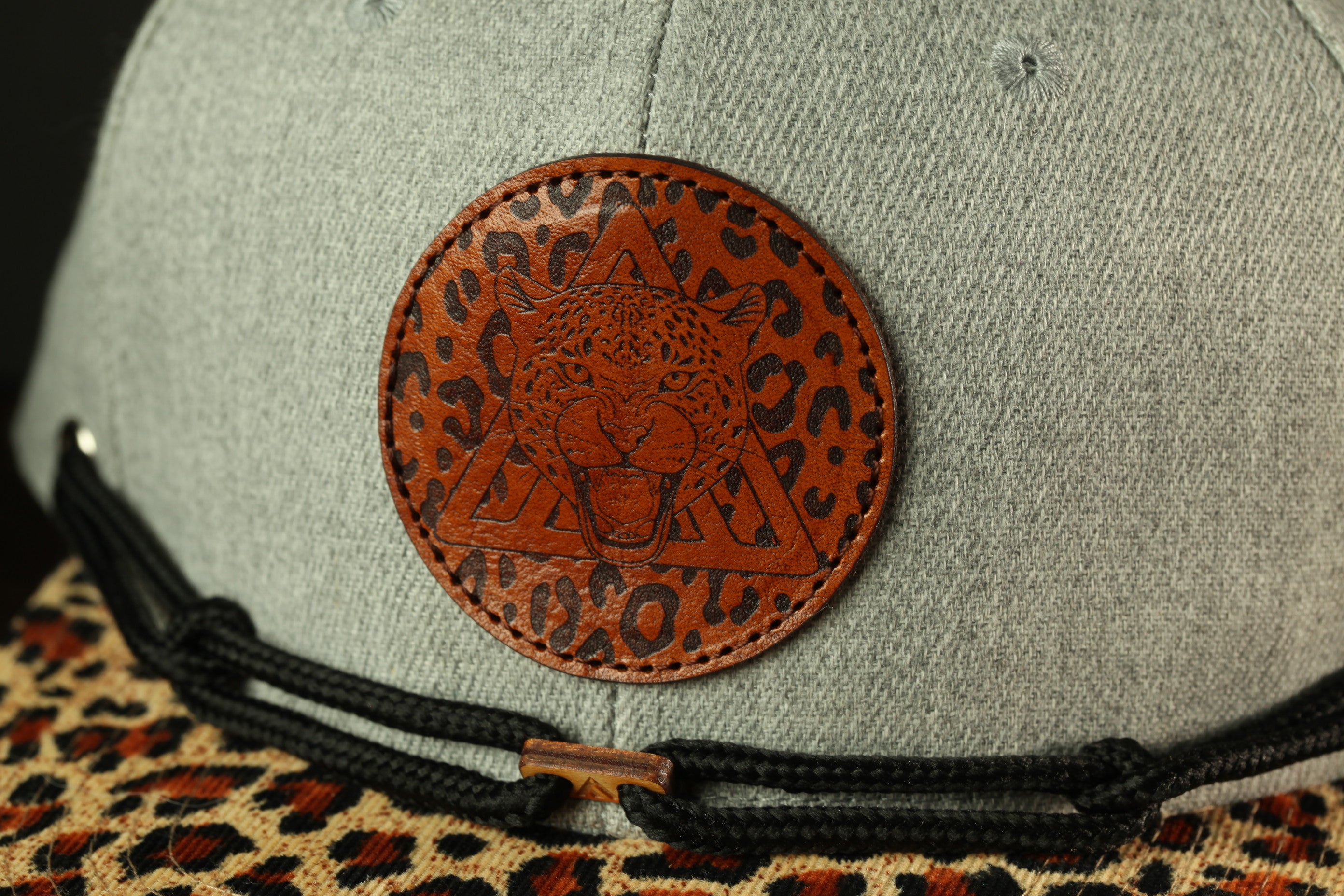 A close-up view of a gray baseball cap with a brown leather patch featuring a leopard print design.
